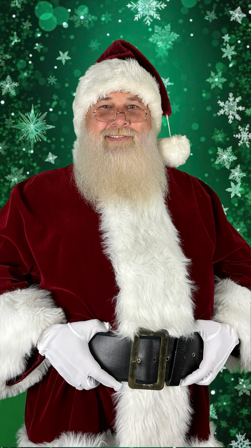 Person dressed as Santa Claus with a white beard, red suit, and hat, standing against a green snowy background.