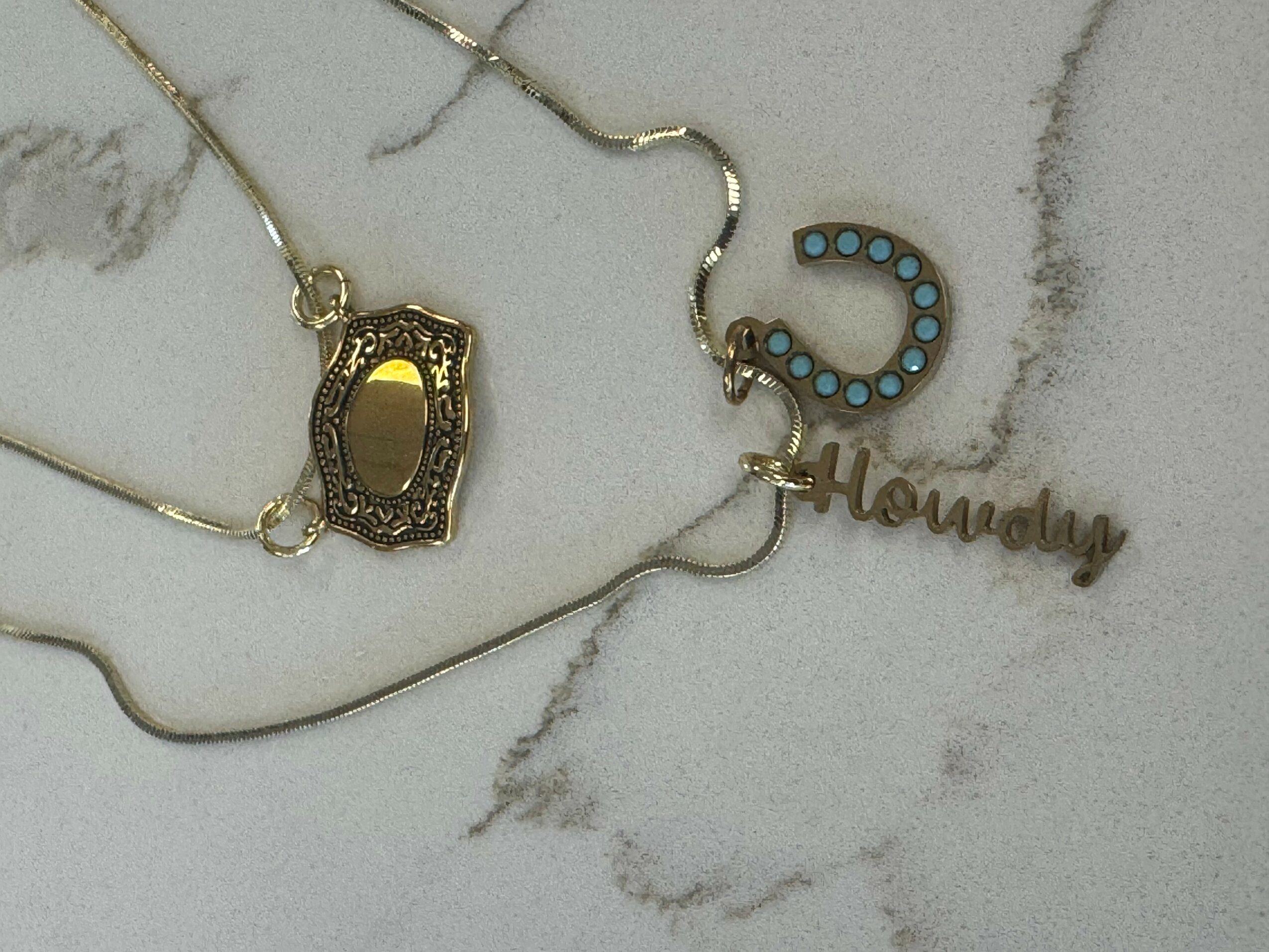 Necklaces with a pendant, a horseshoe, and a nameplate on a marble surface.