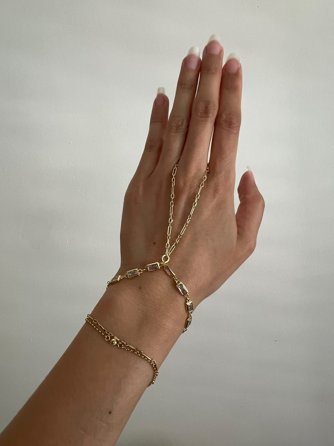 Hand with multiple gold bracelets and a chain draped over fingers, against a plain background.