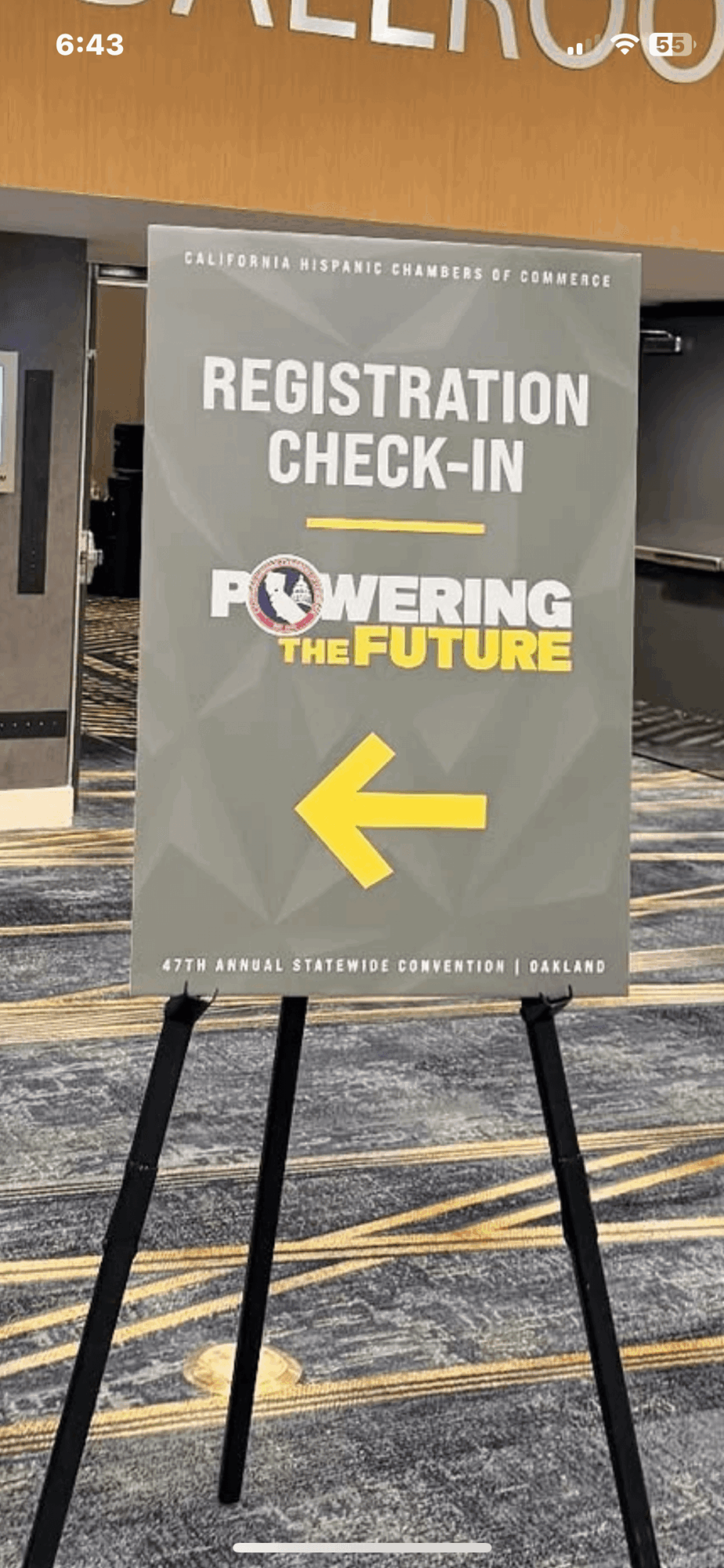 Registration check-in sign with arrow pointing left, text about powering the future, located indoors on a stand.