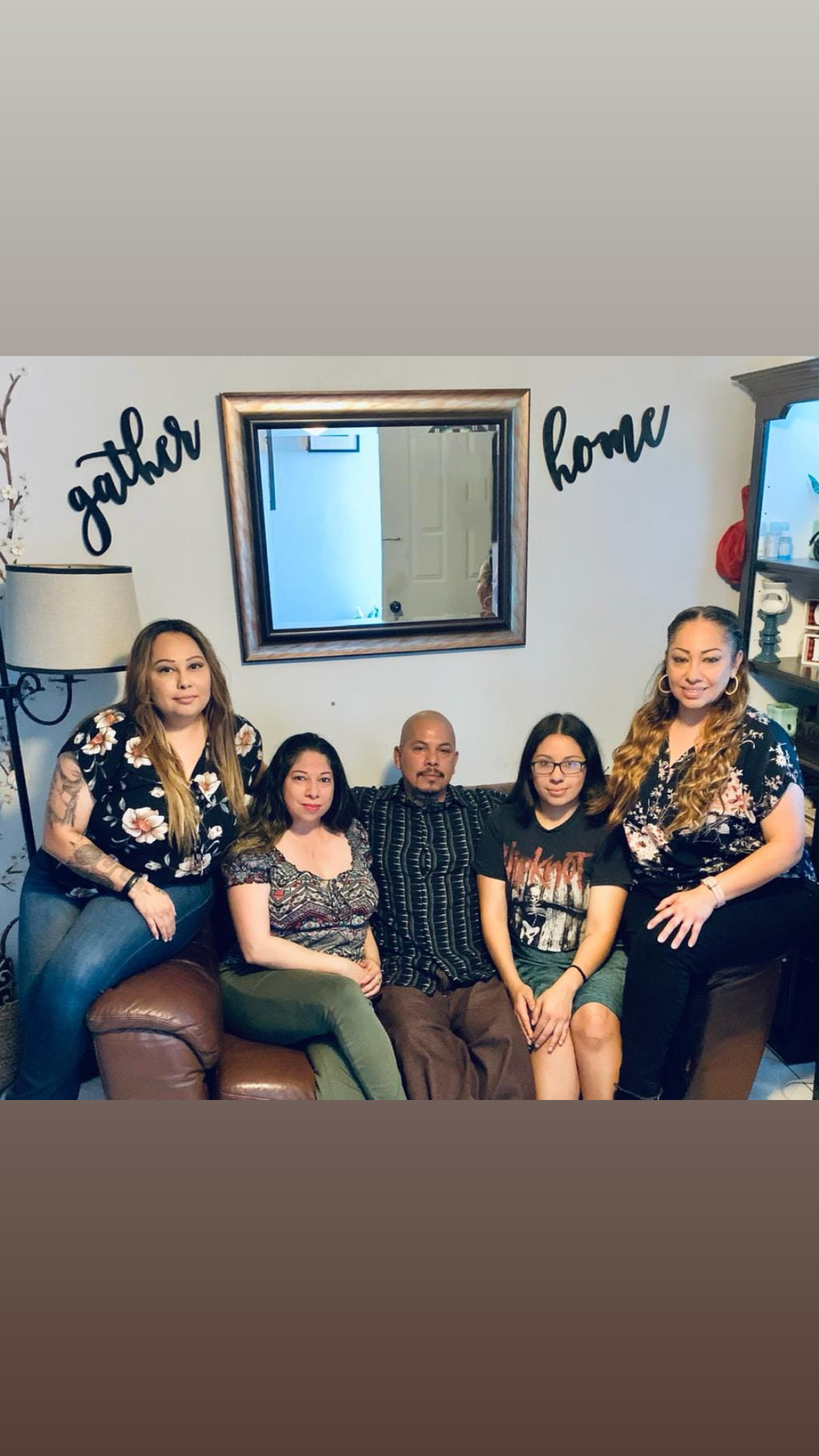 Five people sitting on a couch in a living room, with a mirror and wall decorations behind them.
