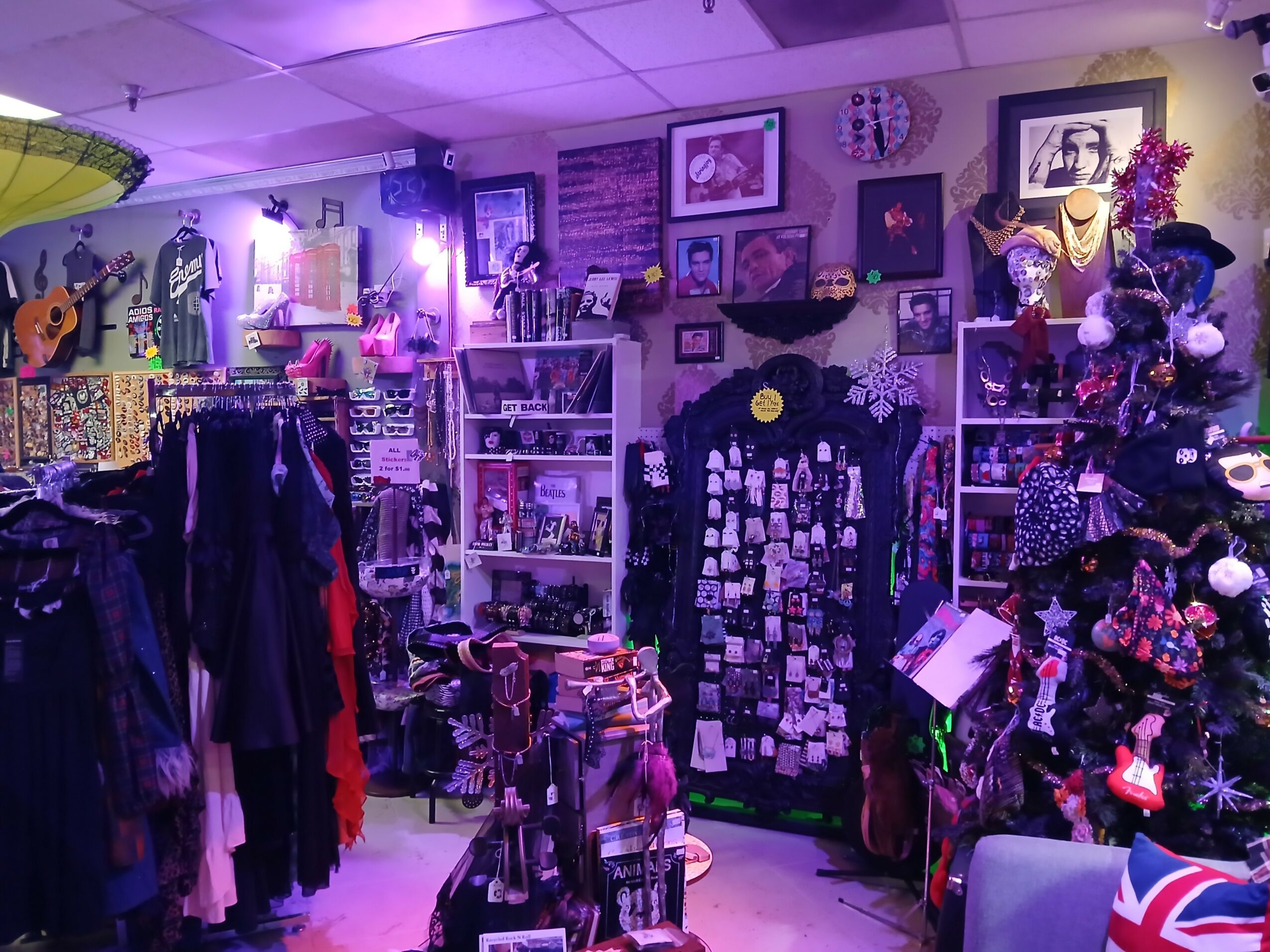 Clothing store with racks of clothes, shelves of accessories, and a decorated Christmas tree, illuminated by purple lighting.