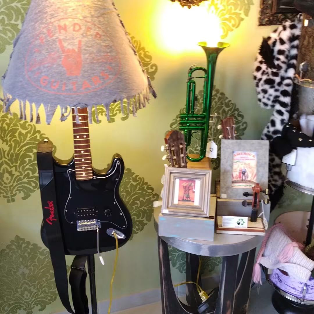 Guitar-shaped lamp, green trumpet, framed pictures, and decorative items on a round table against a green patterned wall.