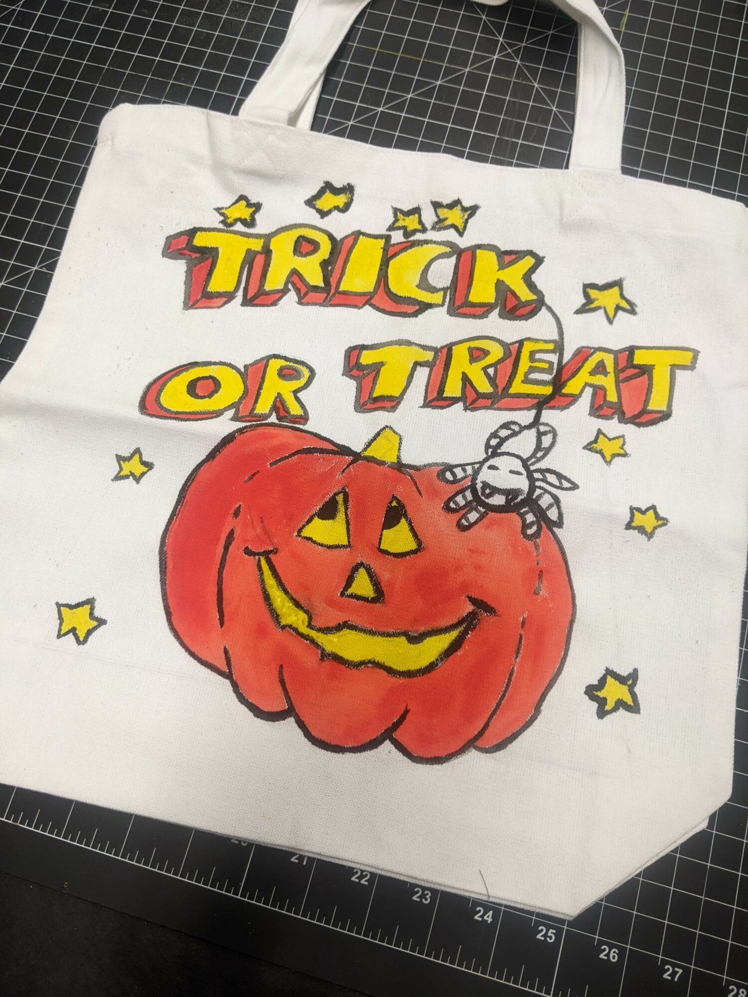 White tote bag with a pumpkin, a spider, and the text 'Trick or Treat' in colorful letters, surrounded by stars.