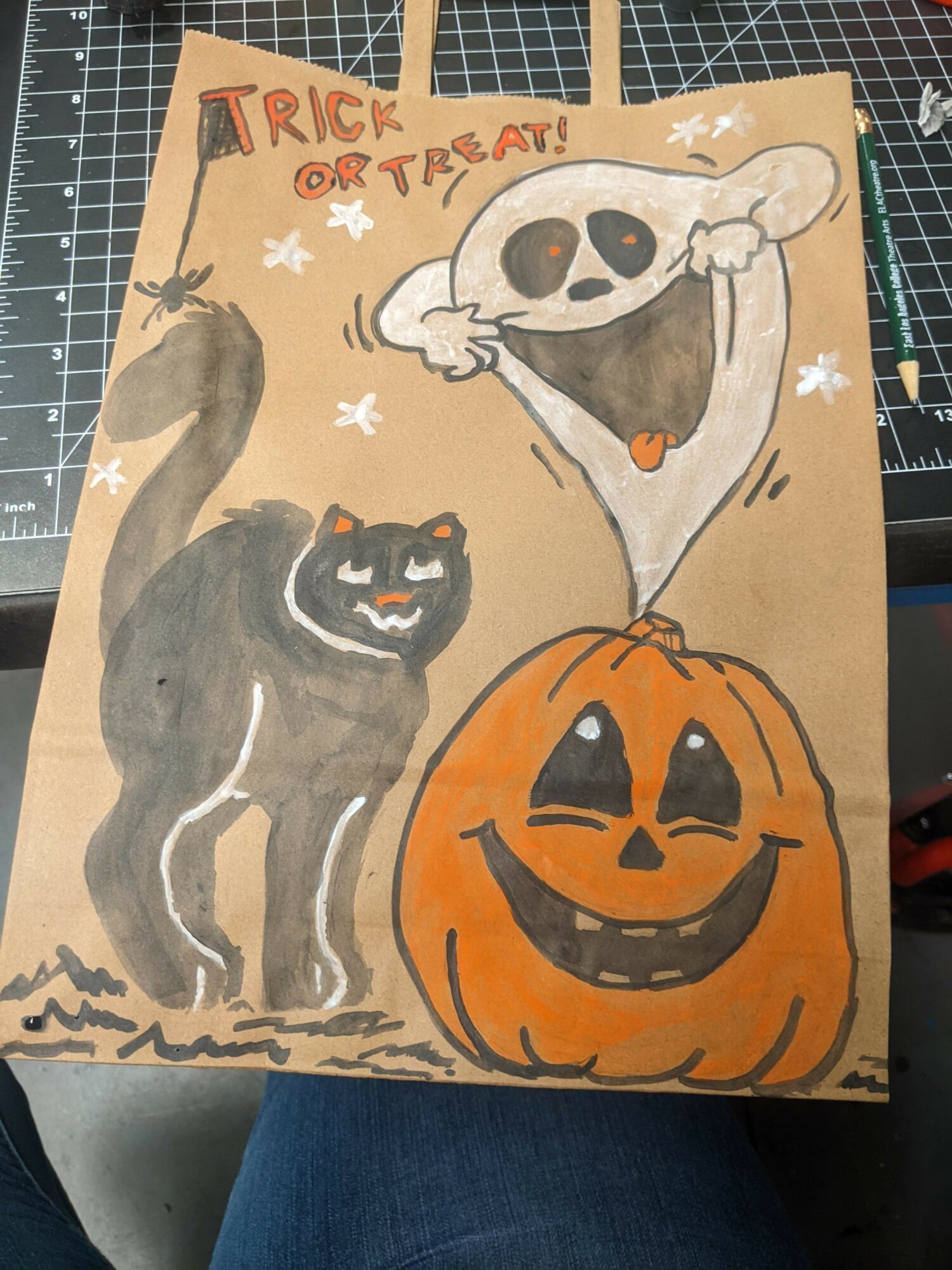 Hand-drawn Halloween scene with a smiling pumpkin, a black cat, and a skull with a tongue, on brown paper.