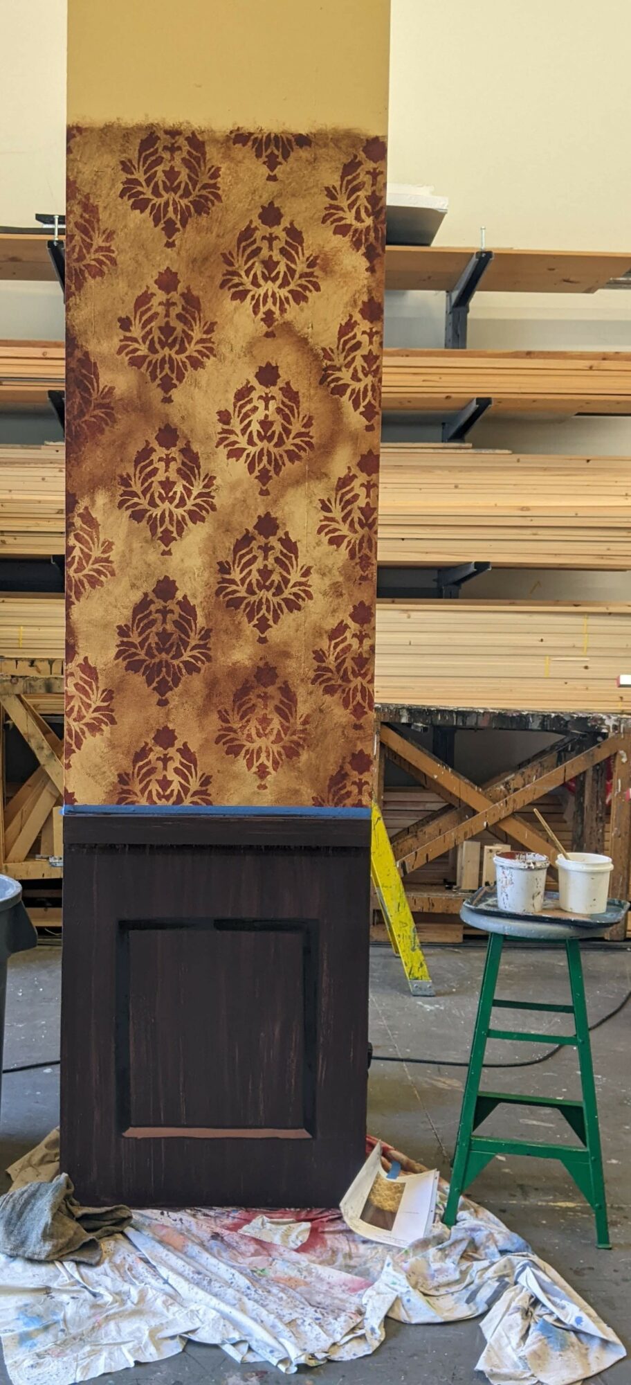 Upright decorative panel with floral pattern above a dark wooden base, placed on a cloth-covered surface in a workshop.