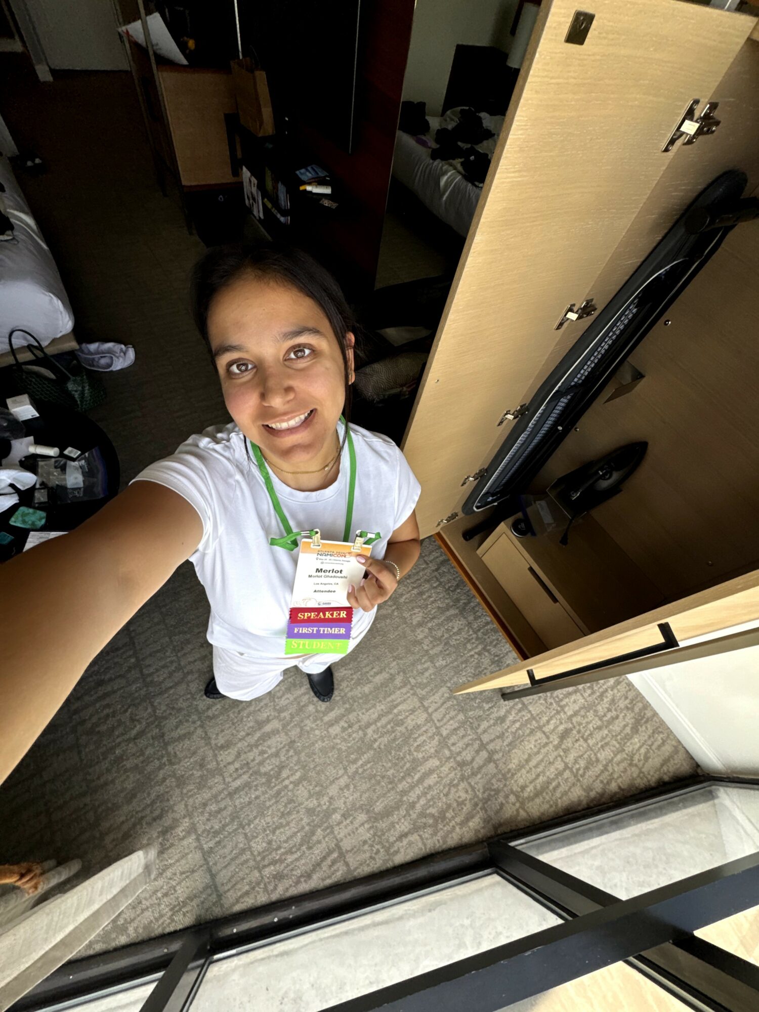 Person taking a selfie in a room, smiling, holding a card, with a mirror and door in the background.