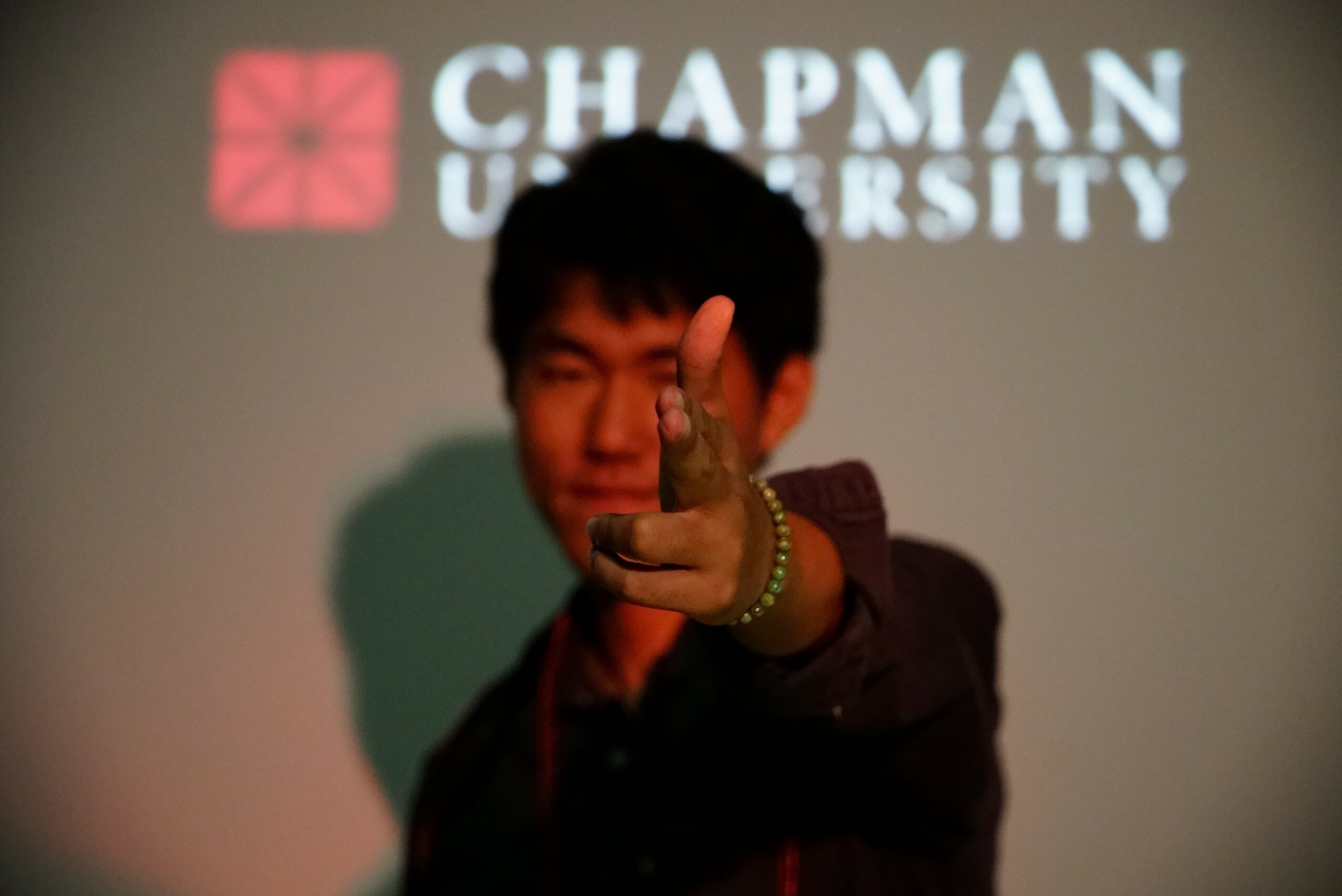 Person pointing towards the camera with a Chapman University logo projected behind them.