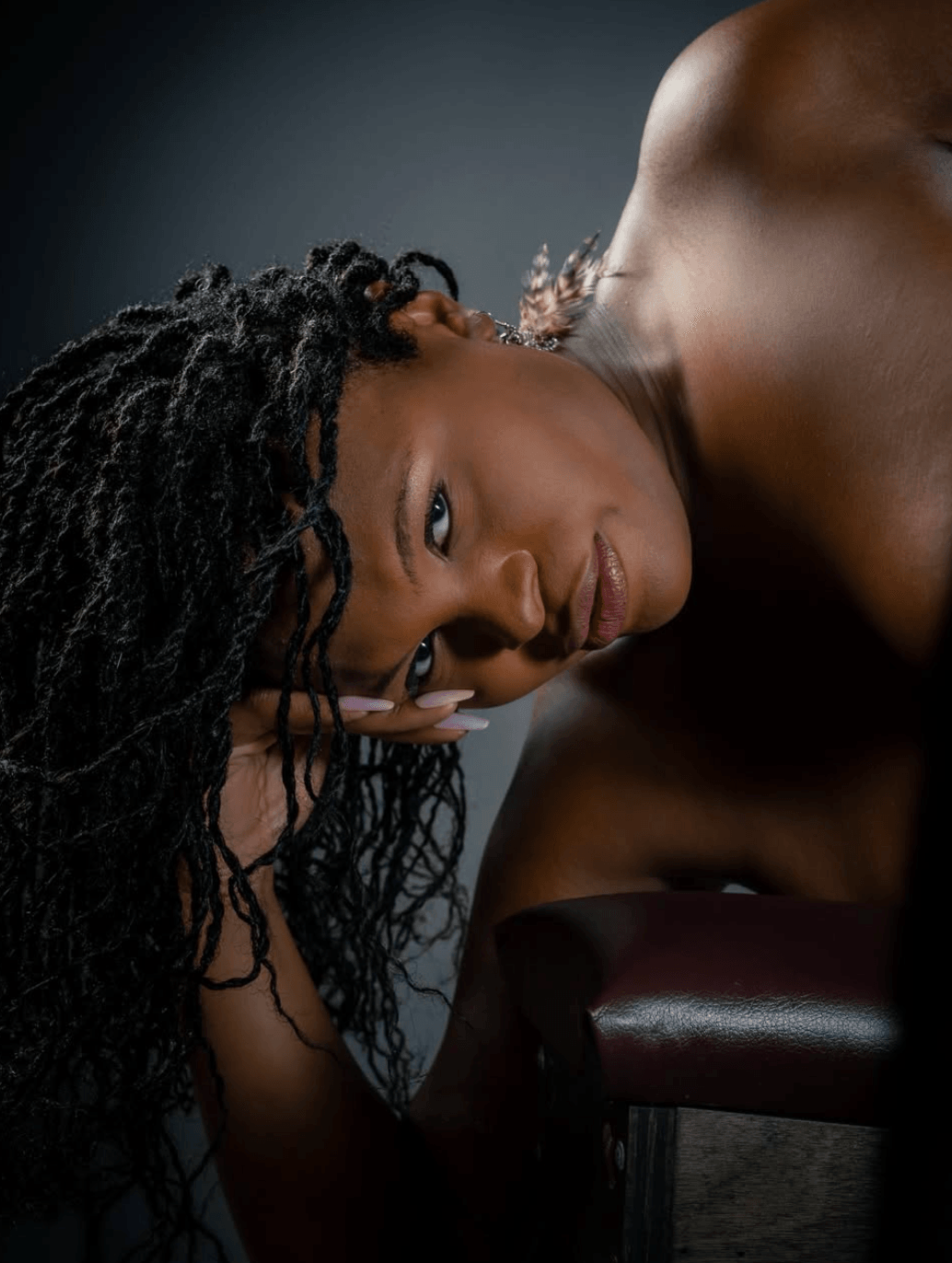 A woman with long, curly hair lying on her side, looking at the camera, with a dark background.