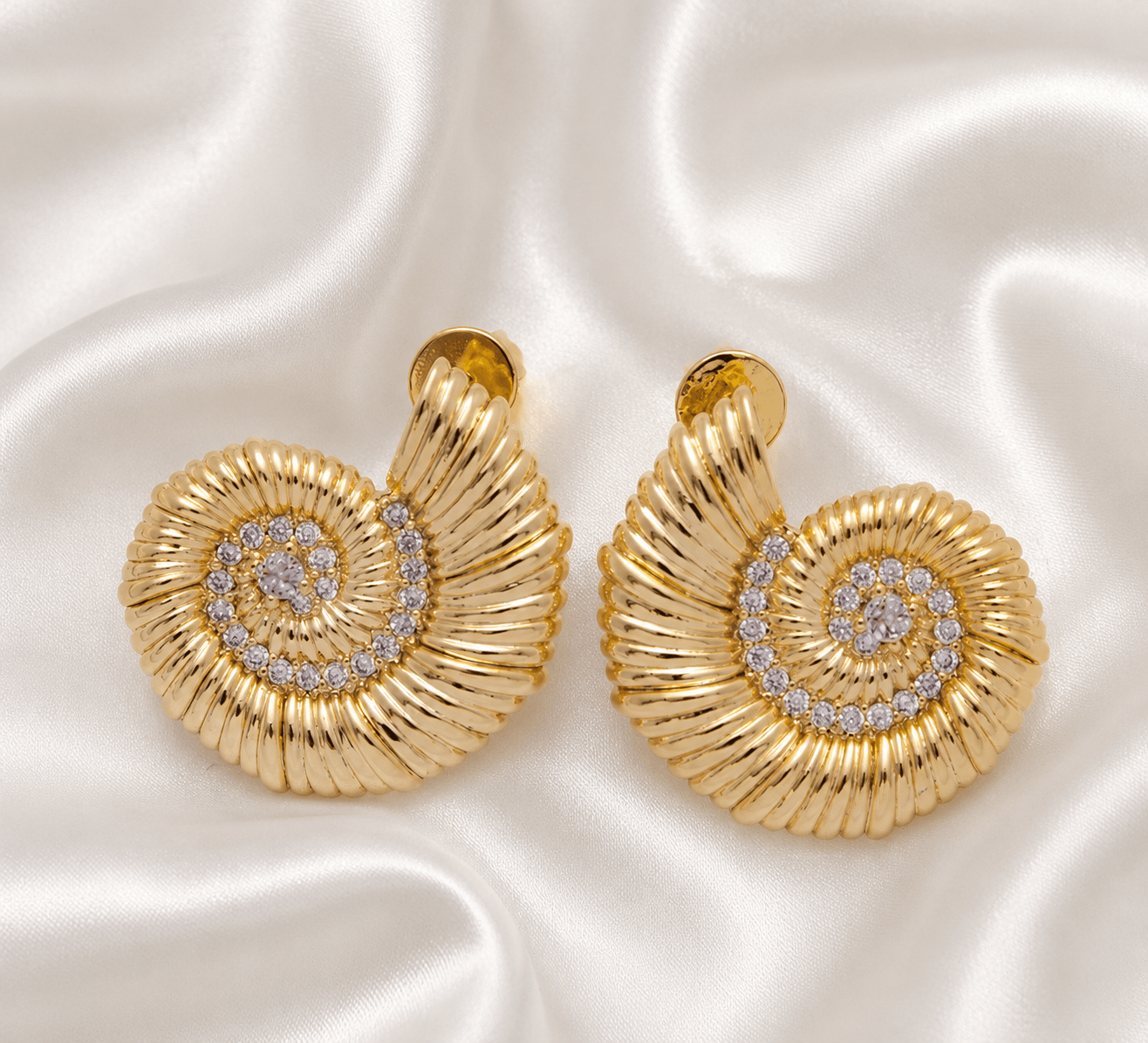 Pair of gold spiral earrings with embedded gemstones on silky white fabric