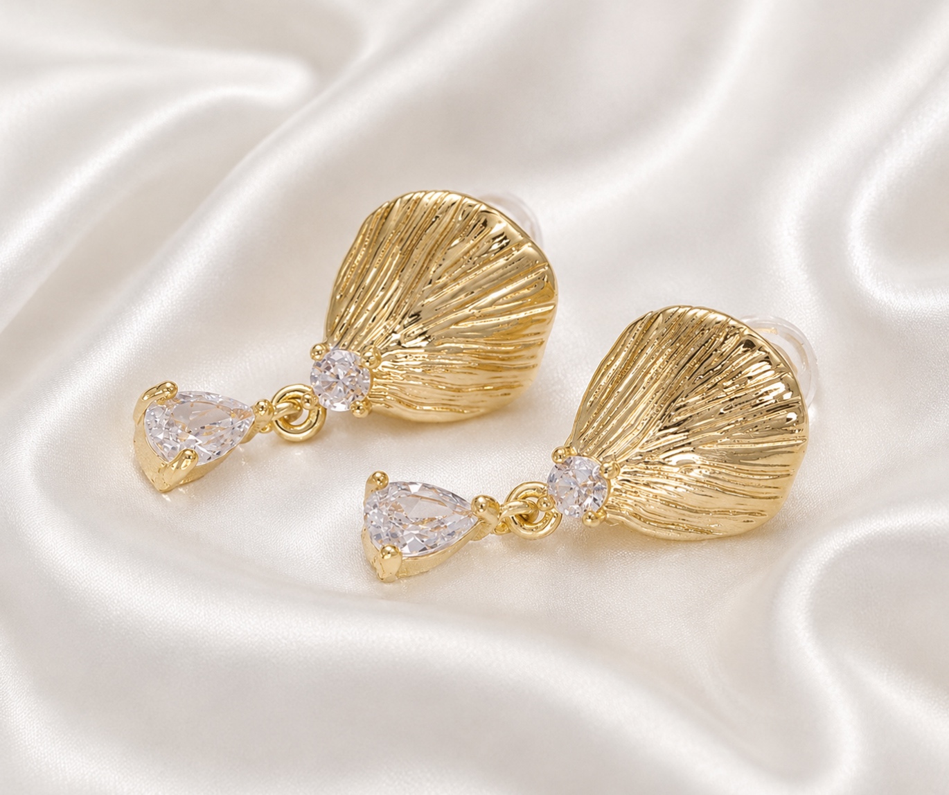 Pair of gold shell-shaped earrings with clear gemstone drops on silky fabric