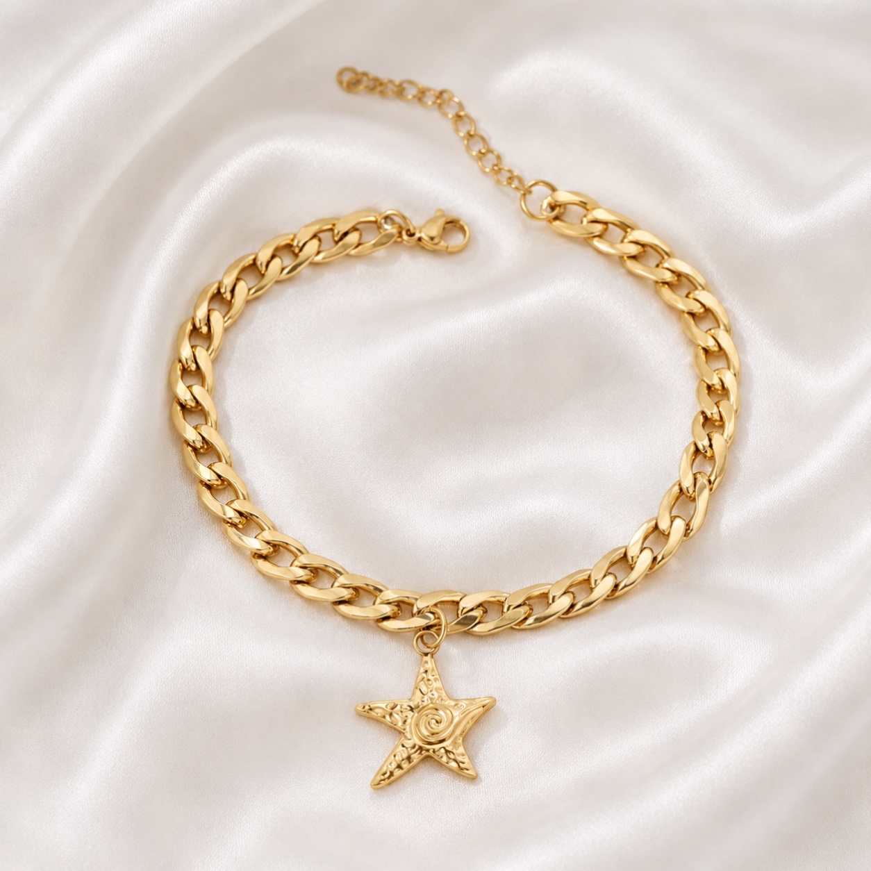 Gold chain bracelet with starfish pendant on white fabric background.