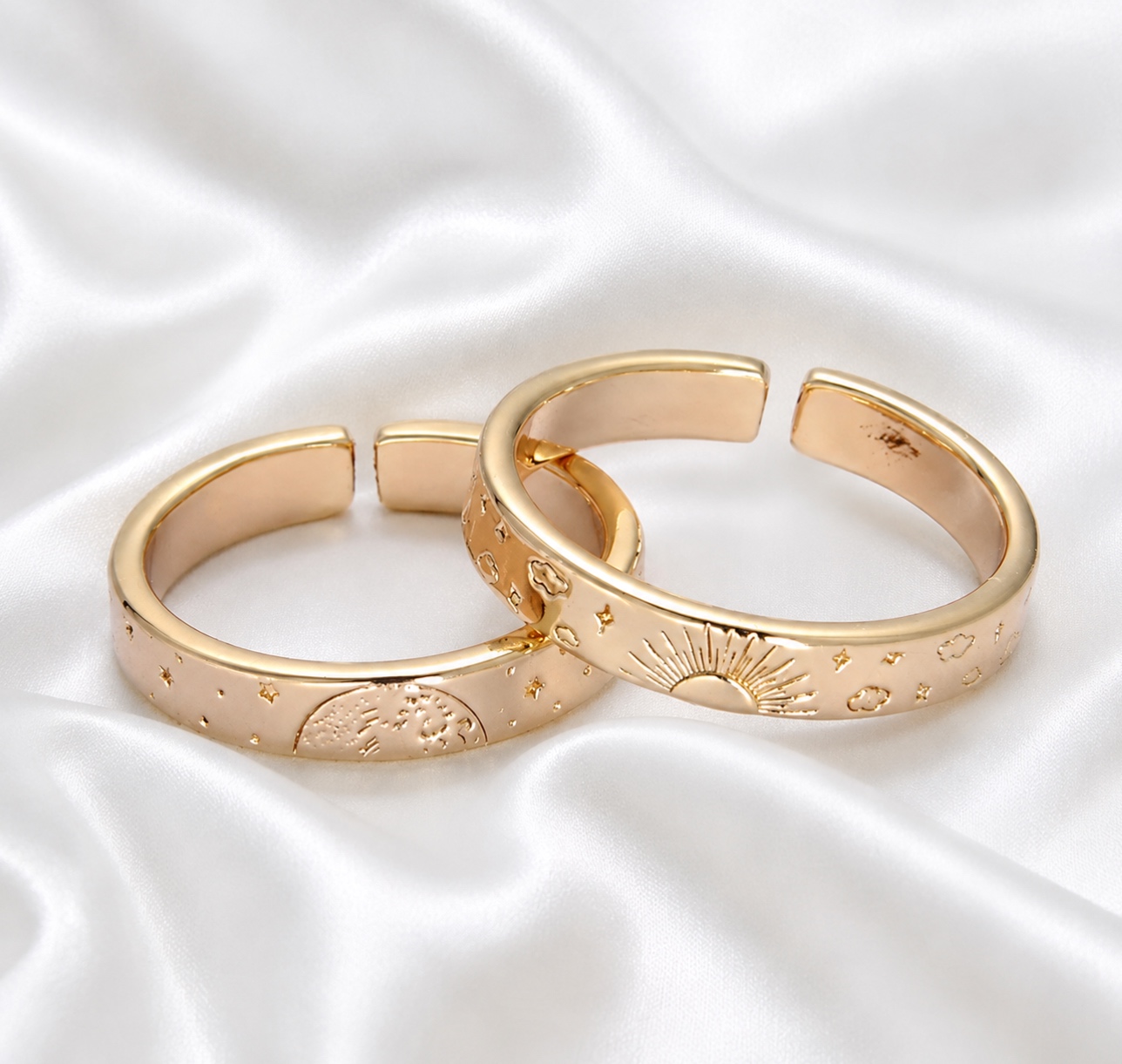 Two gold rings with engraved designs, placed on white satin fabric.