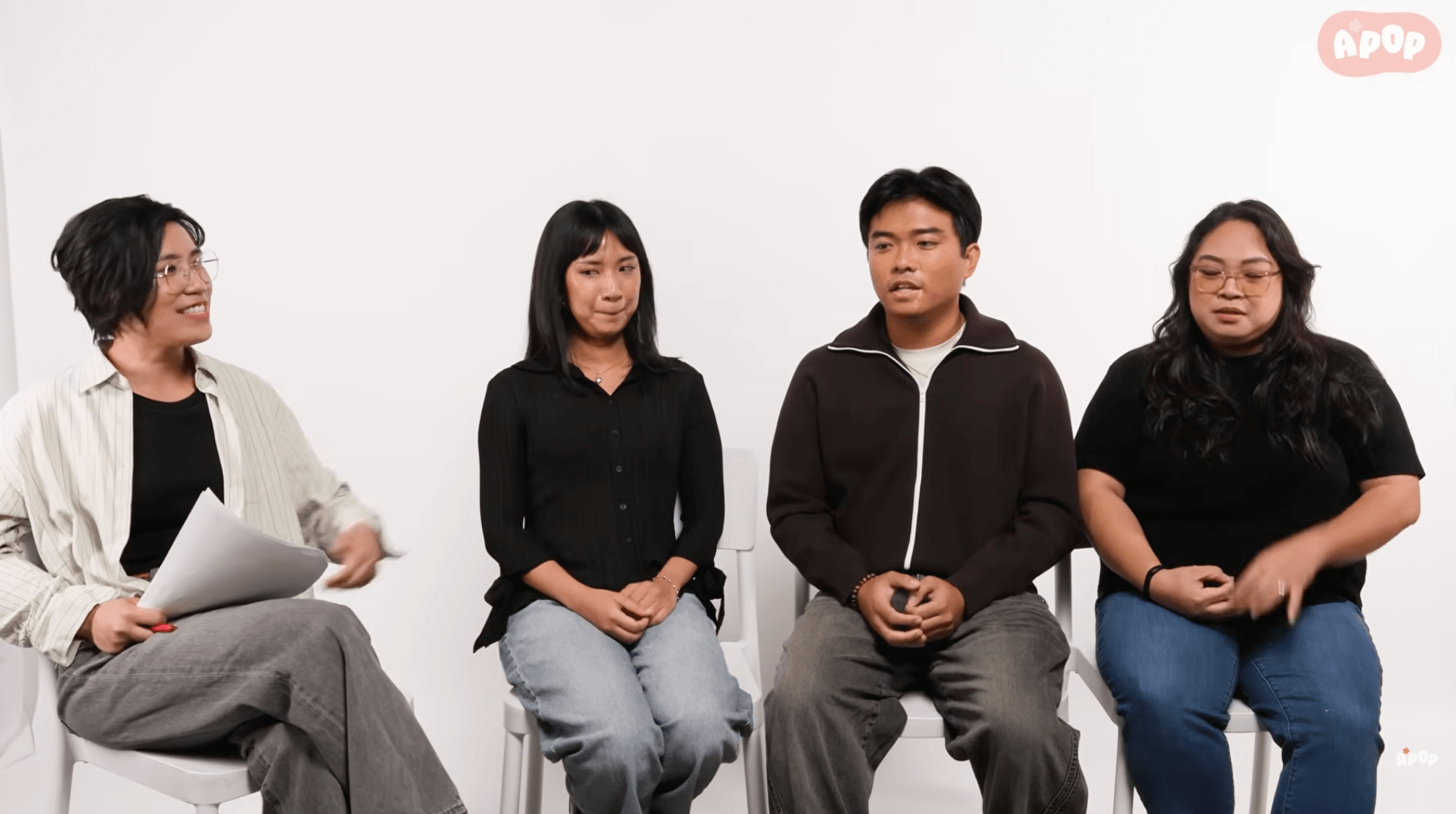 Four people sitting in a row against a white background, engaged in conversation or interview.