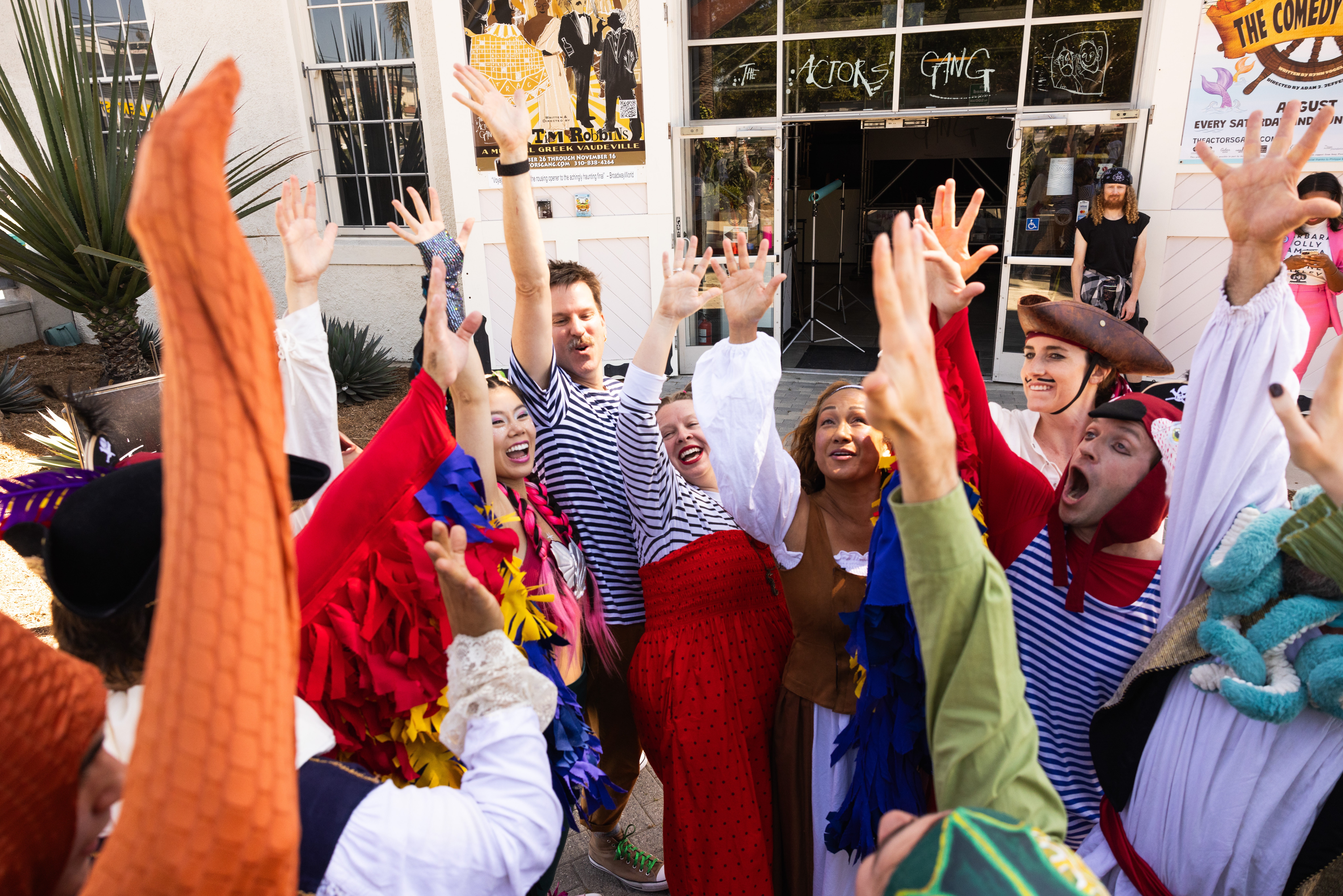 Group of people celebrating outdoors with raised hands, smiling, in colorful costumes and casual clothing.