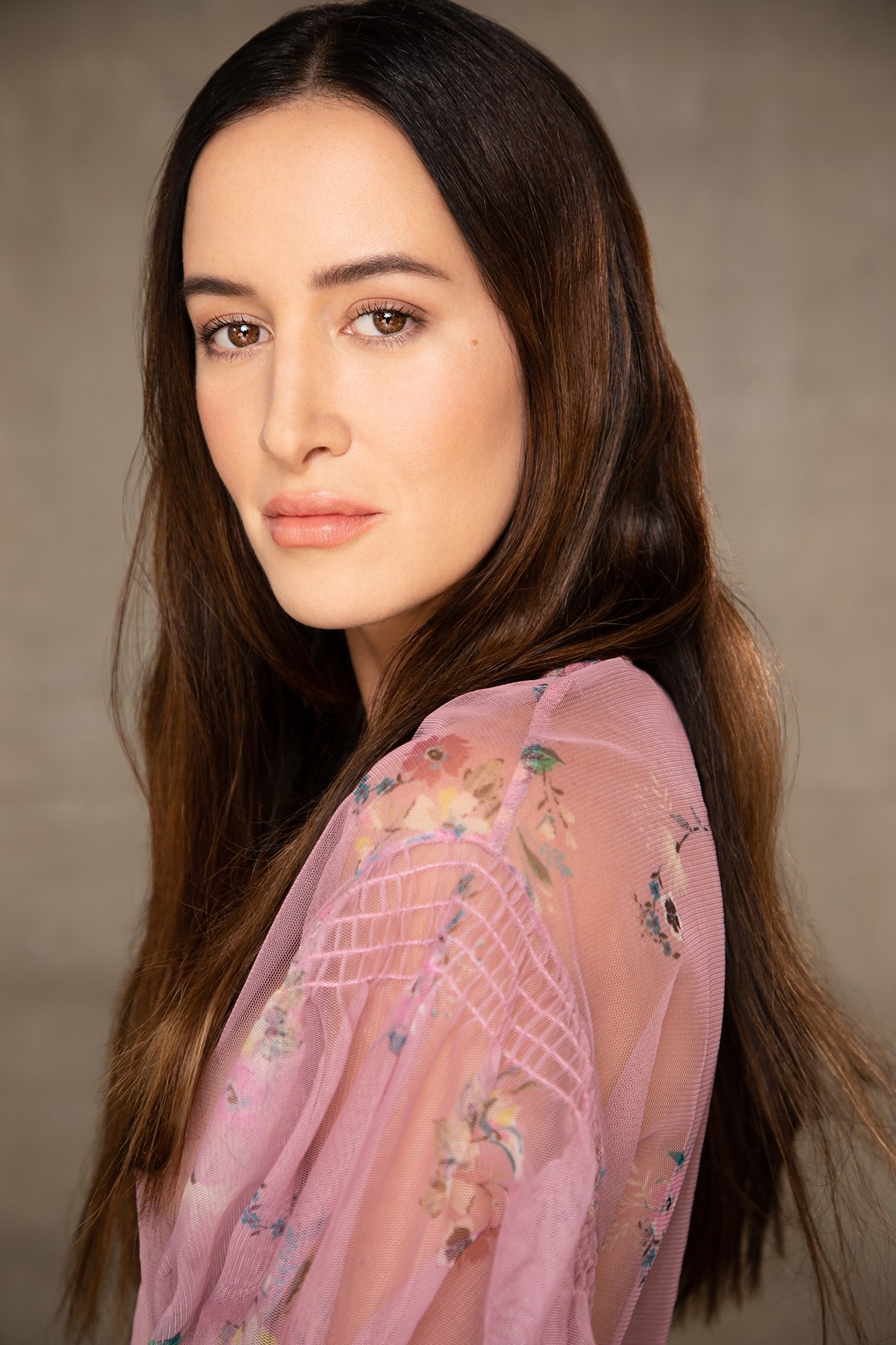 Portrait of a woman with long dark hair, wearing a pink floral top, looking at the camera.