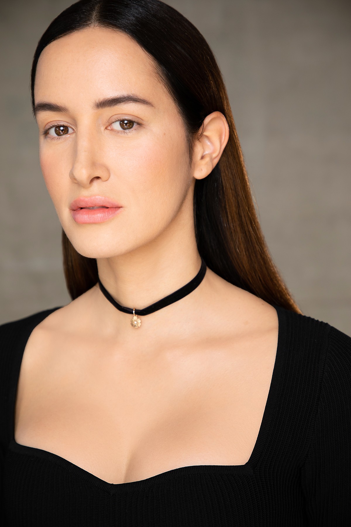 Portrait of a woman with long dark hair, wearing a black choker and black top, against a neutral background.