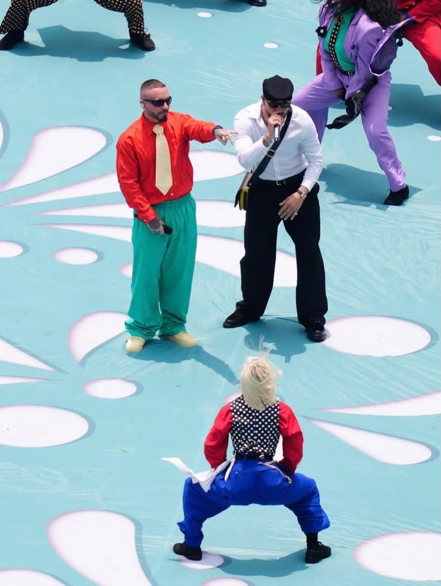Two people in colorful costumes and two in formal attire on a decorated stage, with a person in a clown costume in the foreground.