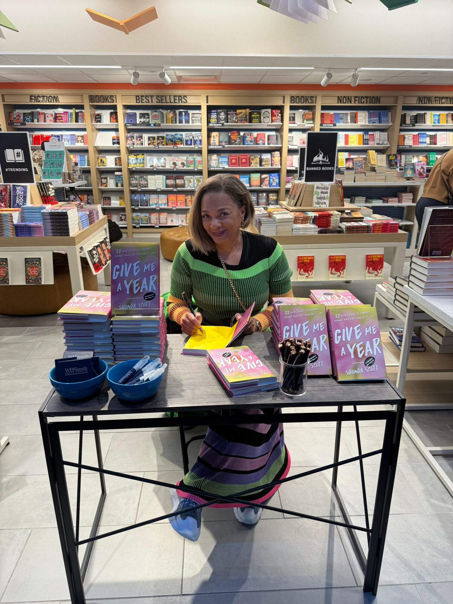 Child sitting at a table in a bookstore, holding a book, with shelves of books in the background.