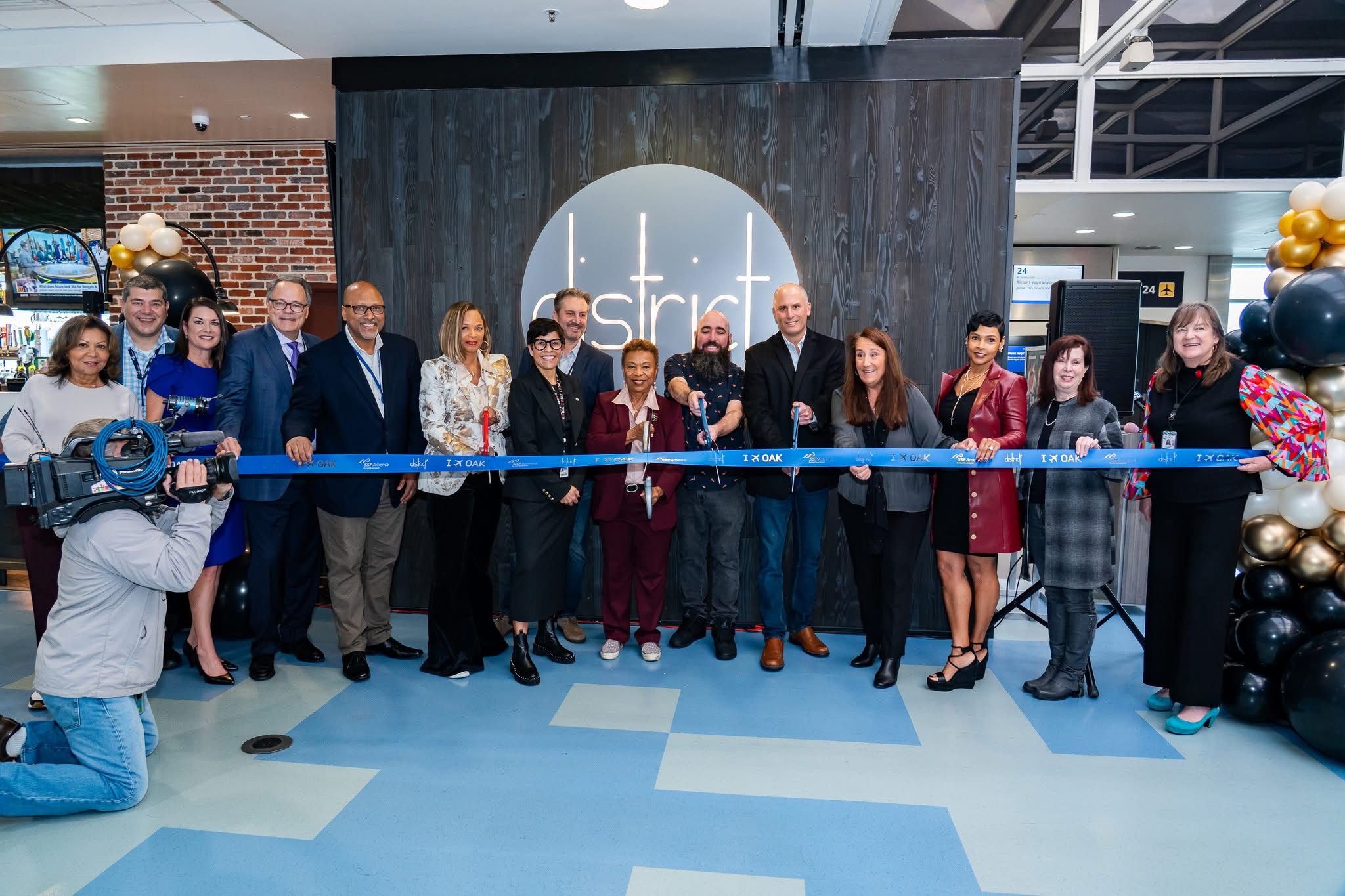Group of people at a ribbon-cutting event in front of a dark wall with a circular logo, some holding scissors, others clapping.