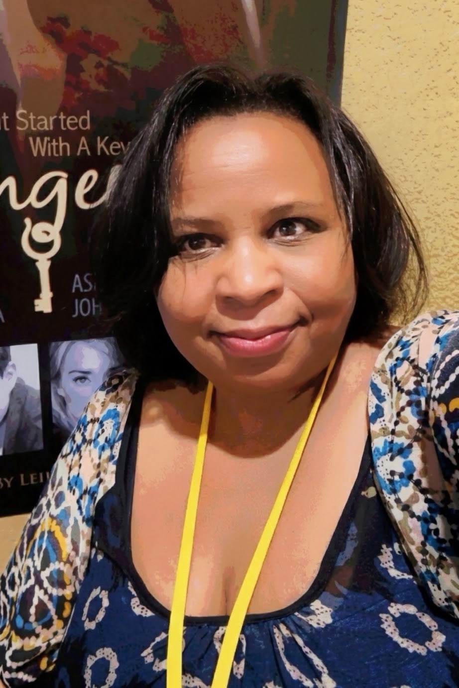 Woman with short dark hair wearing a blue patterned top and yellow lanyard, smiling indoors.