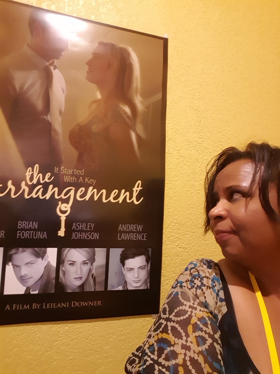Woman with dark hair and patterned top looking at a movie poster on a yellow wall.