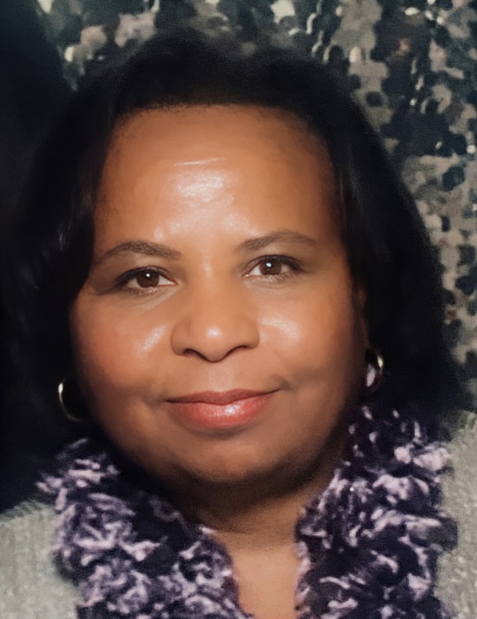 Close-up of a woman with dark hair, wearing earrings and a patterned scarf, smiling at the camera.