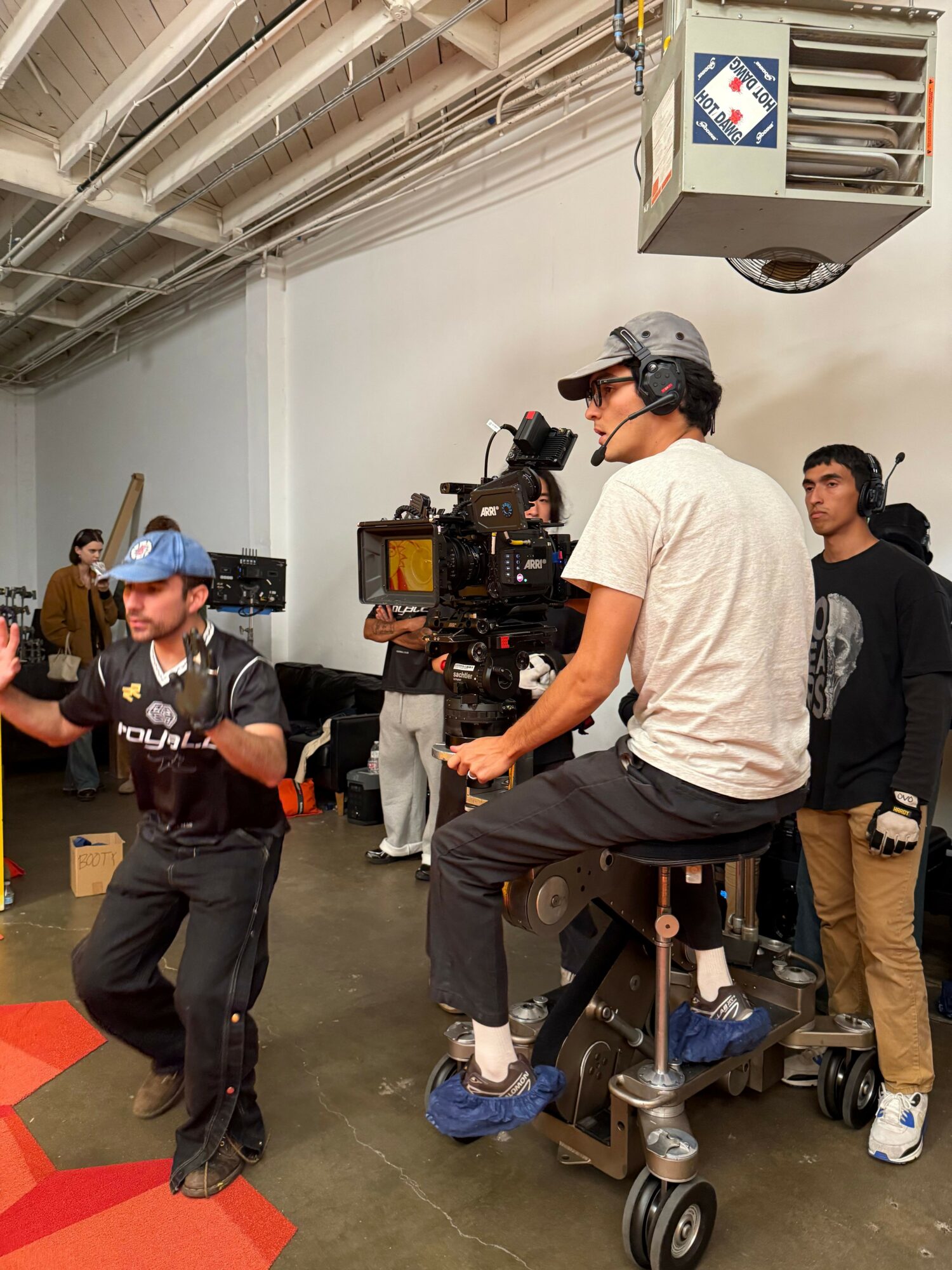 Two people filming with professional camera equipment in an indoor setting, one wearing a helmet and the other in black clothing.