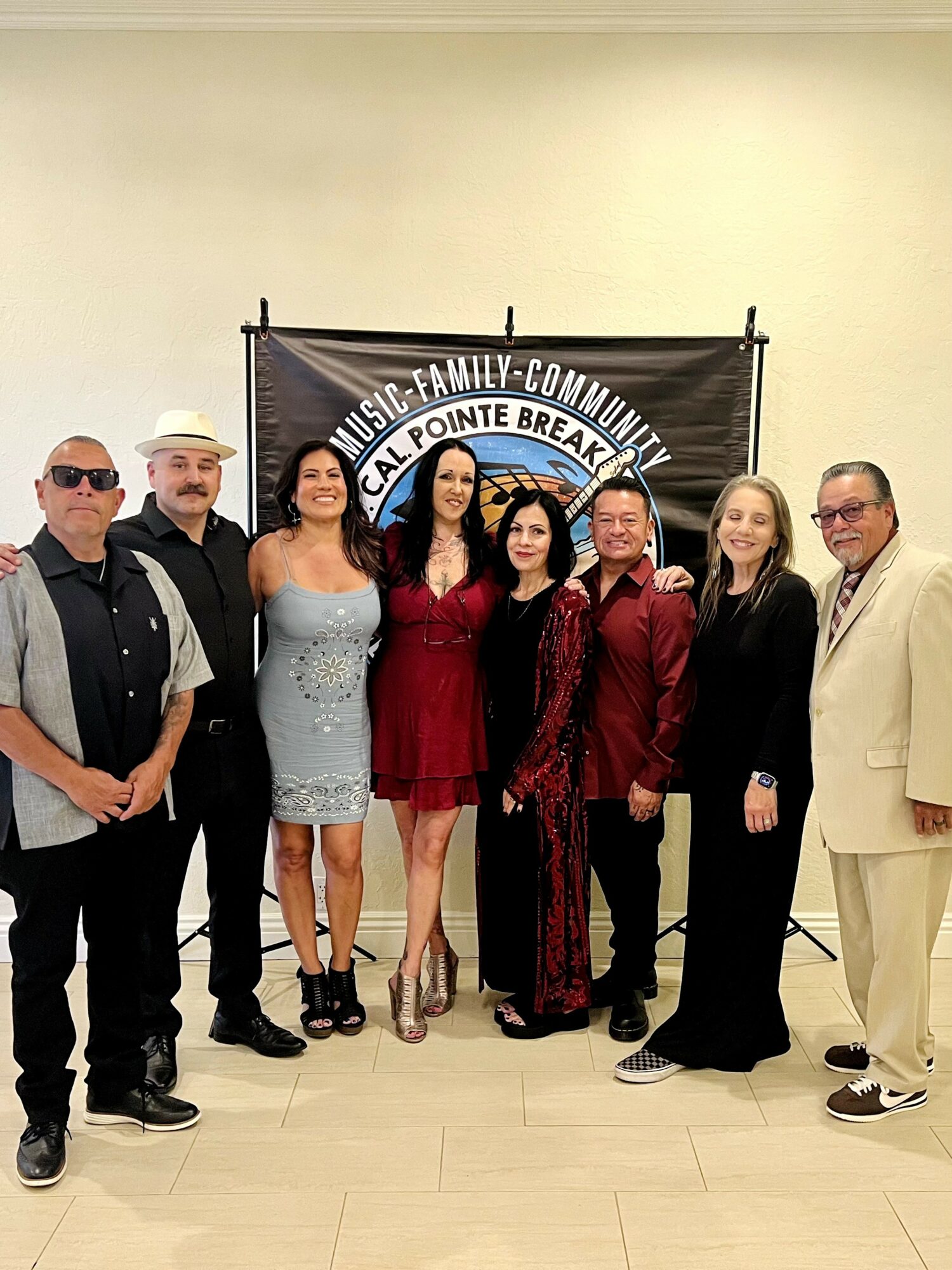 Group of seven people standing in front of a banner, dressed in formal and semi-formal attire, smiling.
