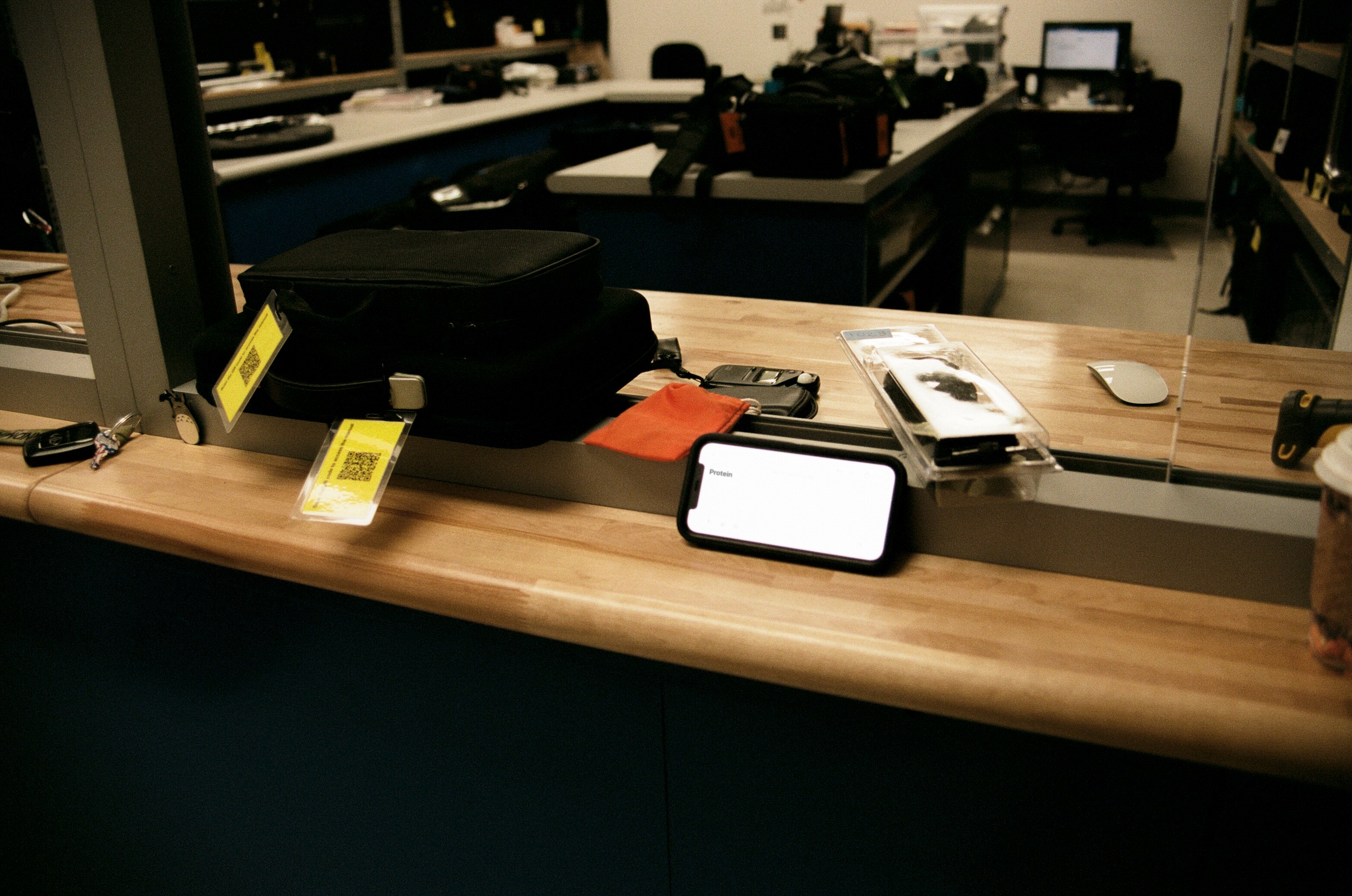 Counter with a smartphone, a red notebook, and a black device in a room with desks and computers in the background.