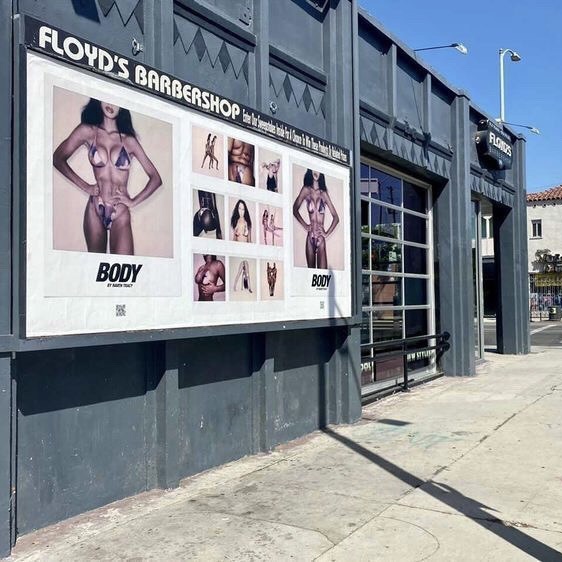 Signboard outside Floyd's Barbershop displaying various images of women in provocative poses, mounted on a dark building exterior.