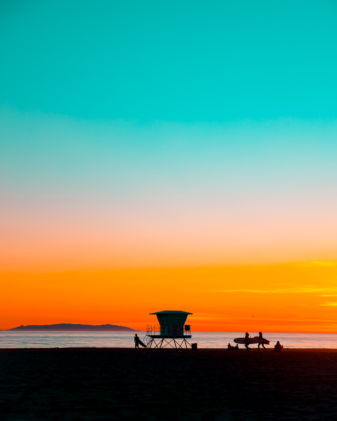 Sunset over water with a lifeguard tower and boats on the beach, colorful sky with orange, pink, and blue hues.