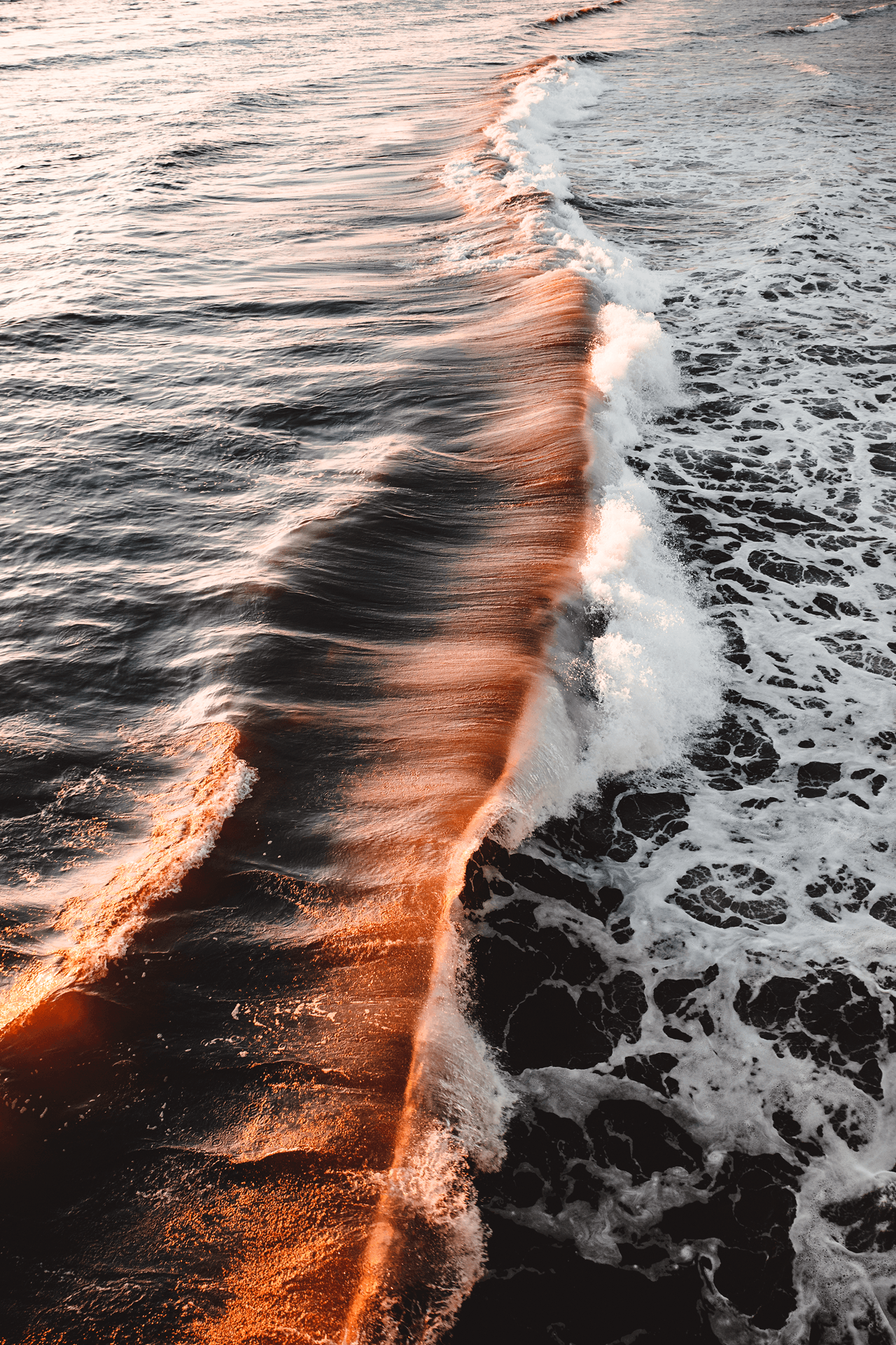 Ocean waves with sunlight reflecting, showing a wake pattern with foam and ripples, viewed from above.