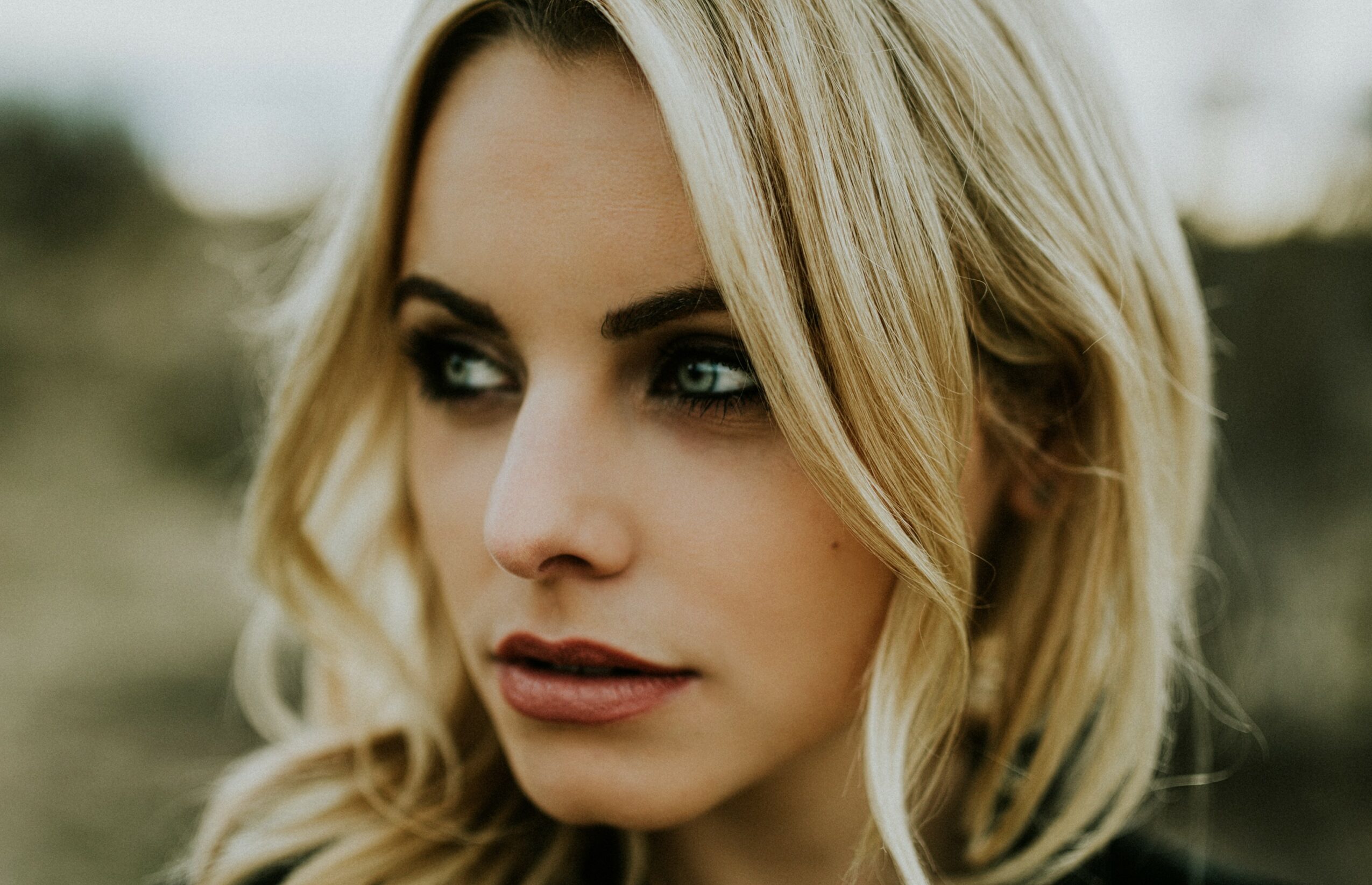 Close-up of a woman with blonde hair and makeup outdoors, looking to the side.