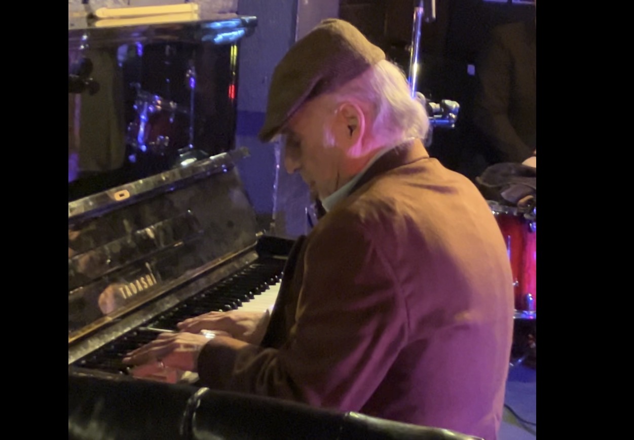 Person wearing a hat playing piano in a dimly lit setting.