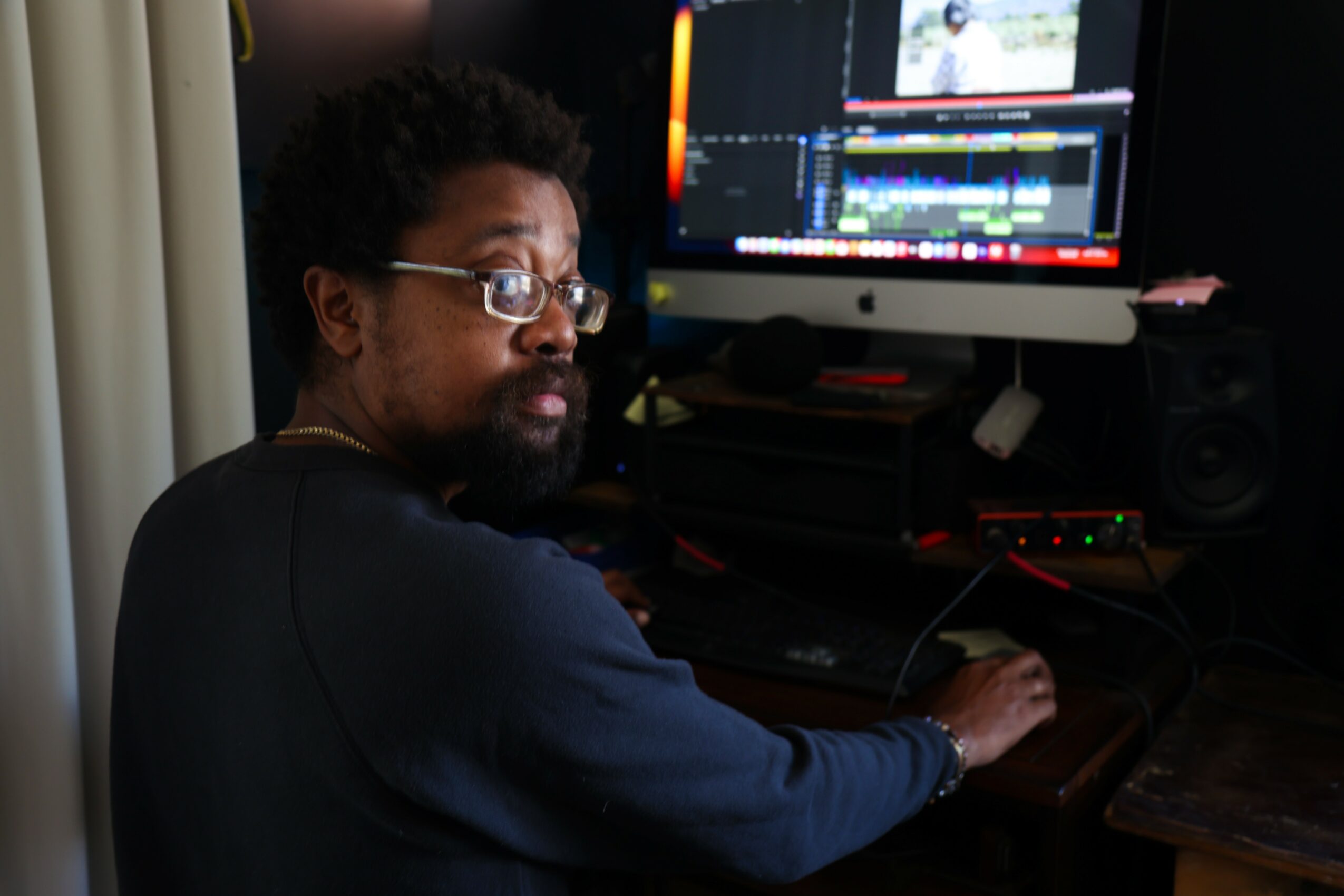 Person with glasses and curly hair working on a computer with a video editing program open.