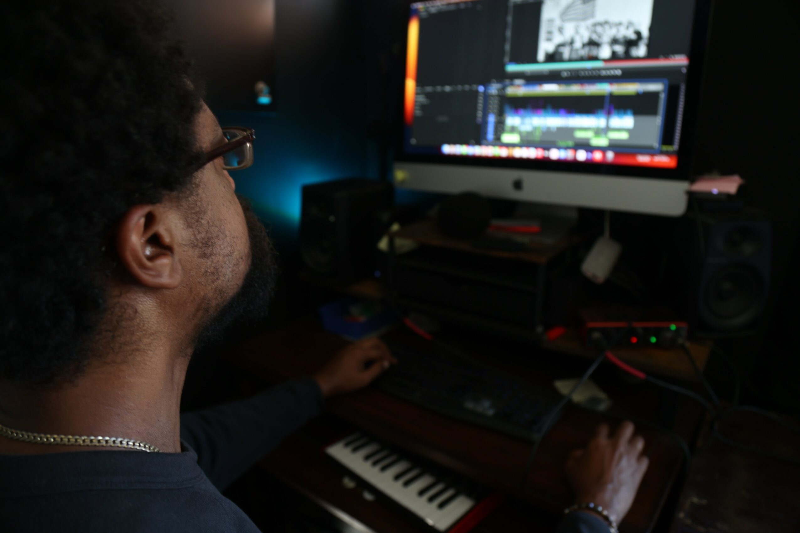 Person working on video editing software on a computer with a keyboard and speakers in a dark room.