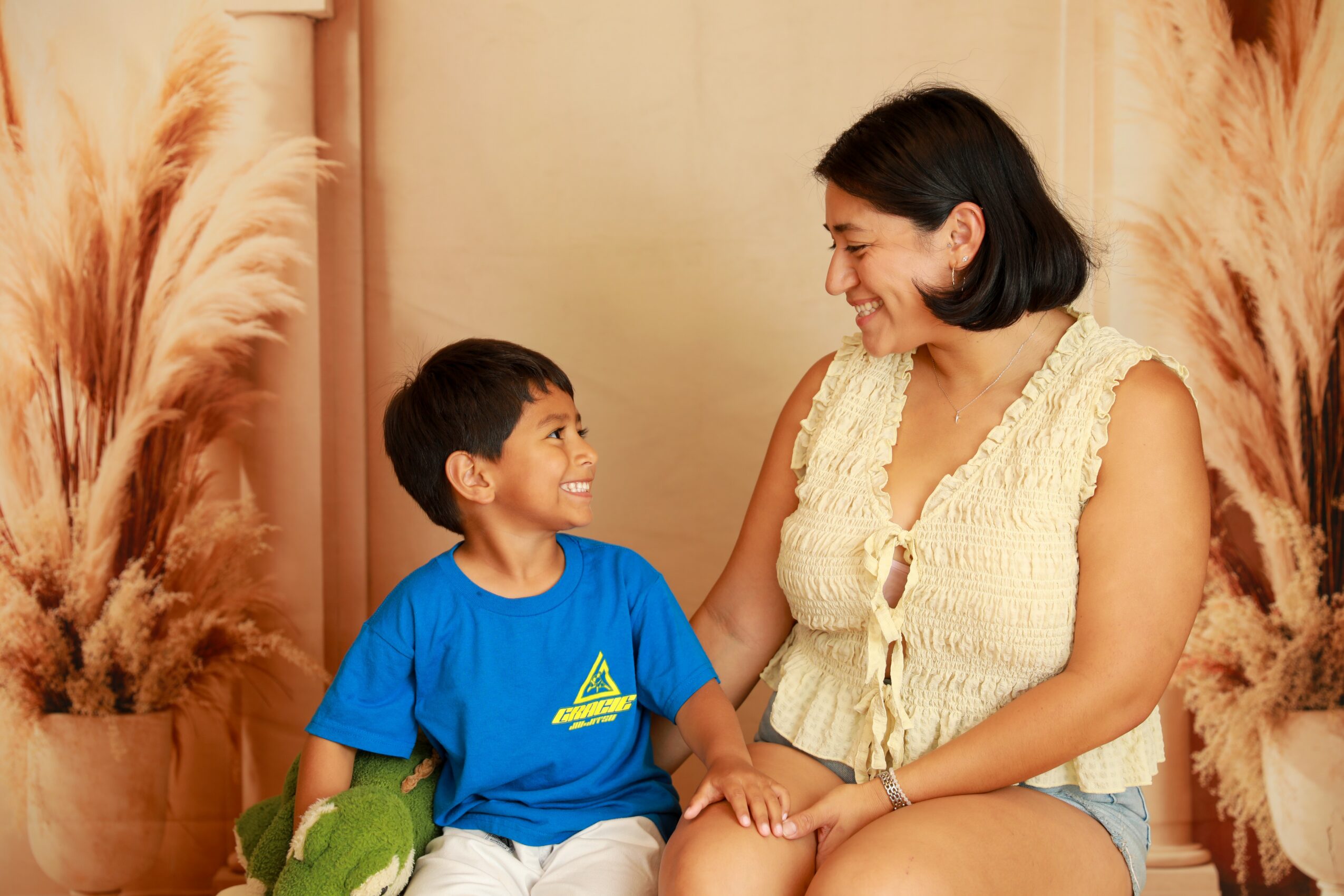 Woman and boy smiling and holding hands indoors with decorative plants in background.