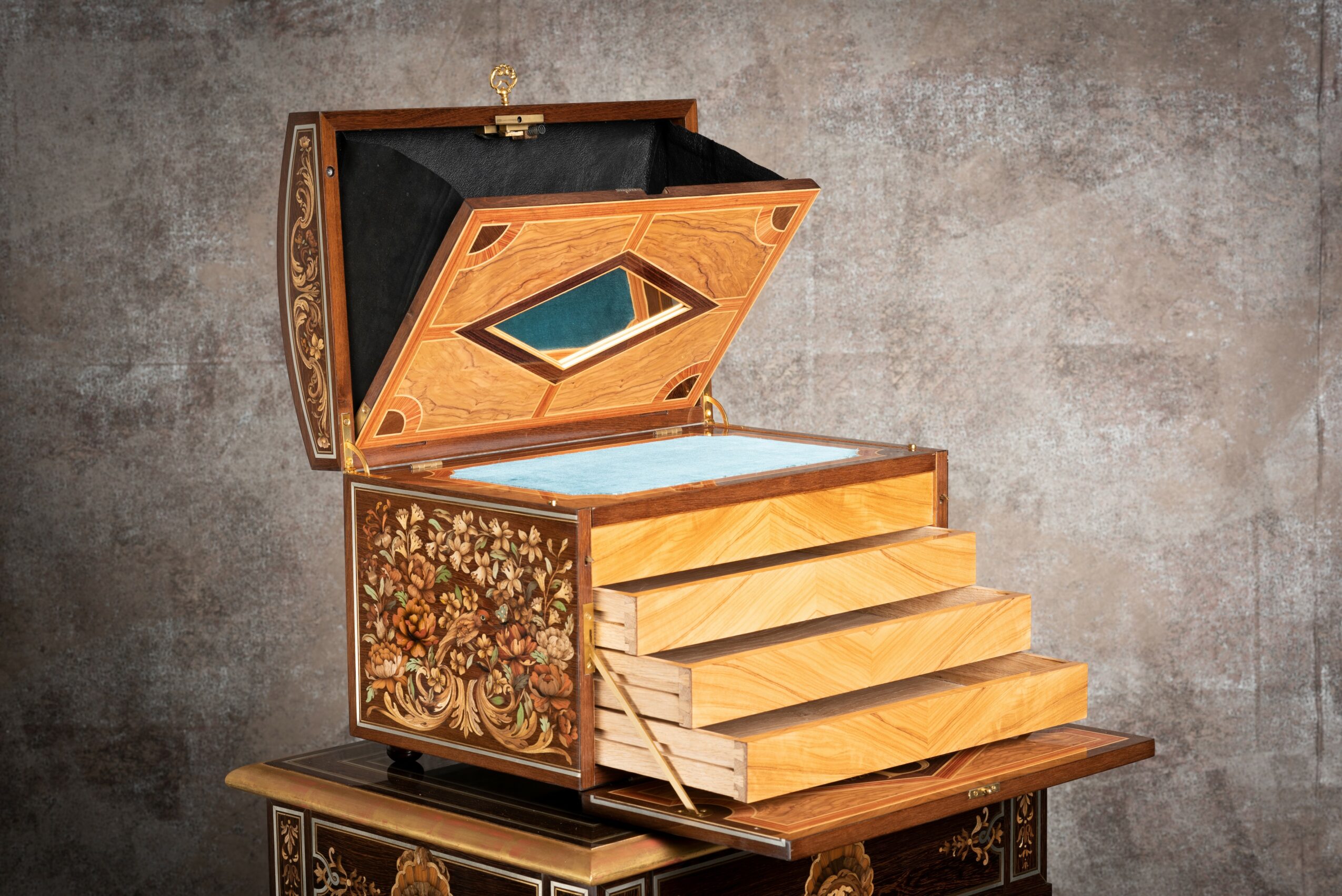 Decorative wooden box with drawers, open lid revealing interior, set against a textured gray background.