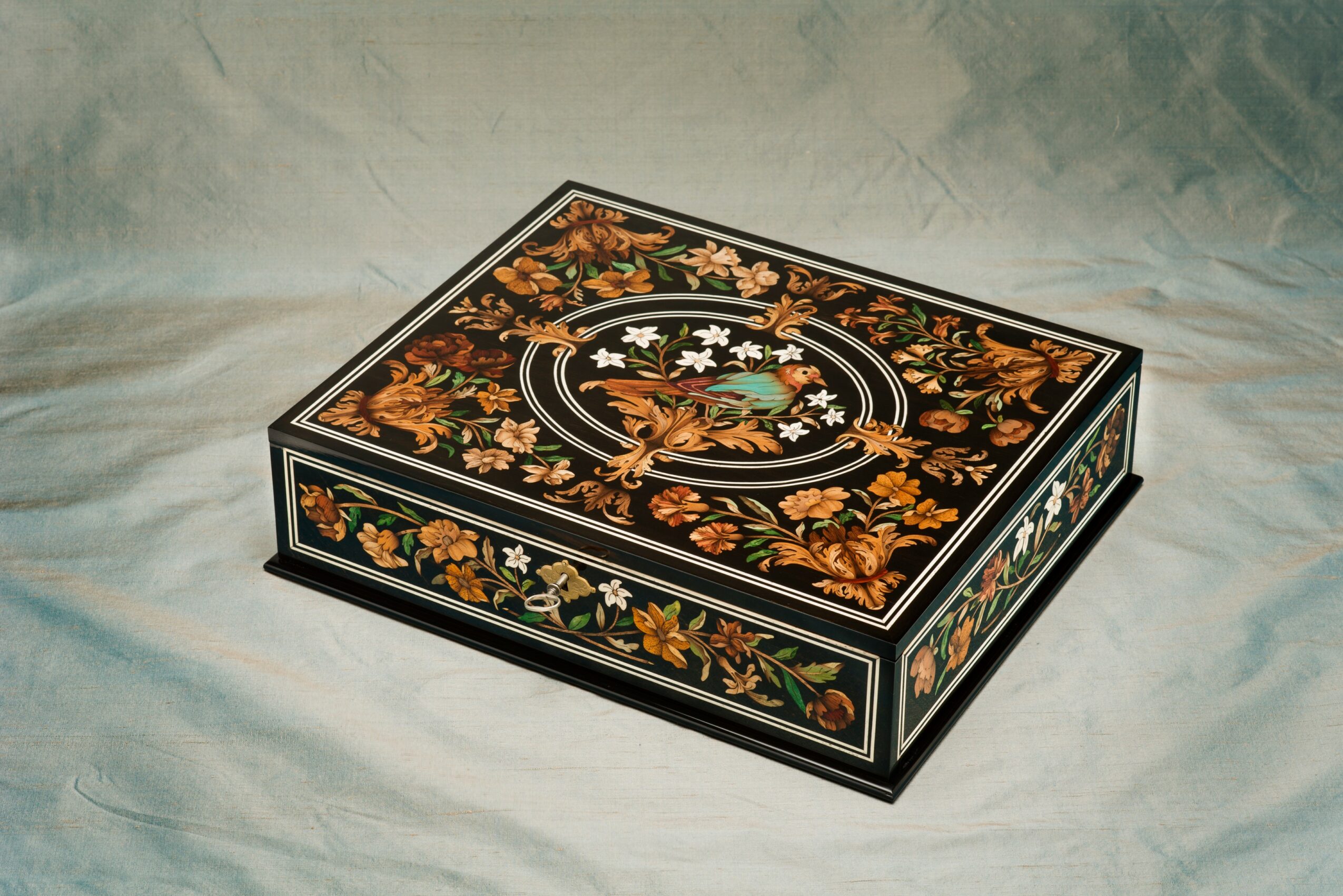 Decorative rectangular box with floral patterns and a central oval design, placed on a fabric surface.