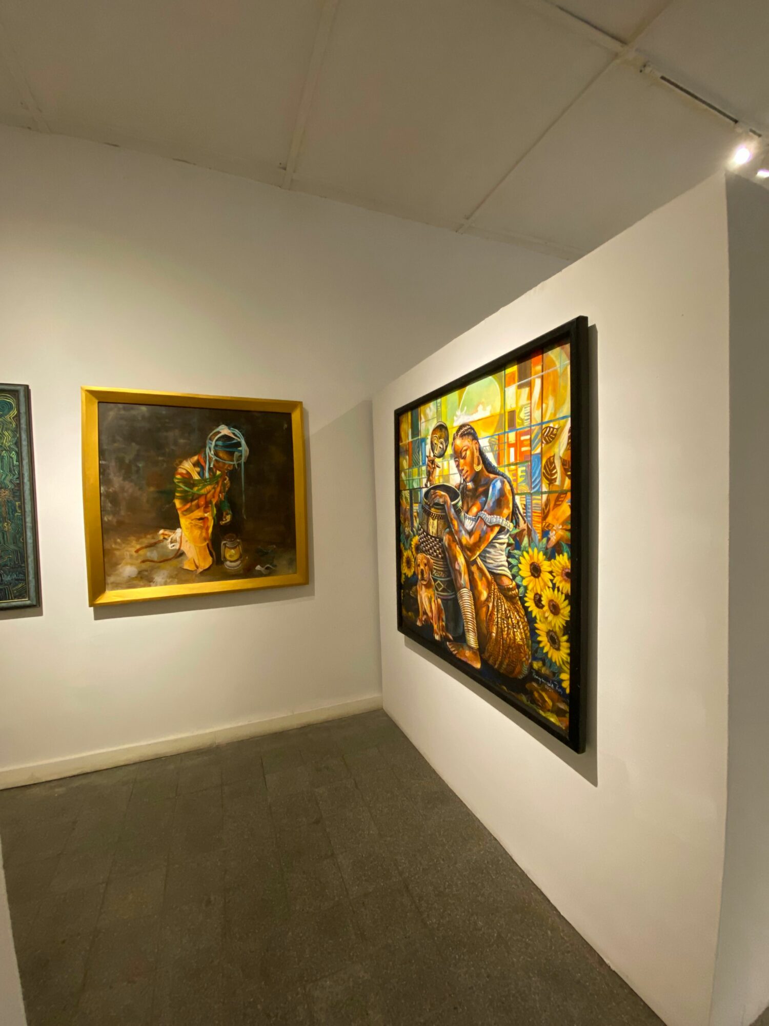 Two framed artworks on white walls, one colorful and one darker, in an art gallery or exhibition space.