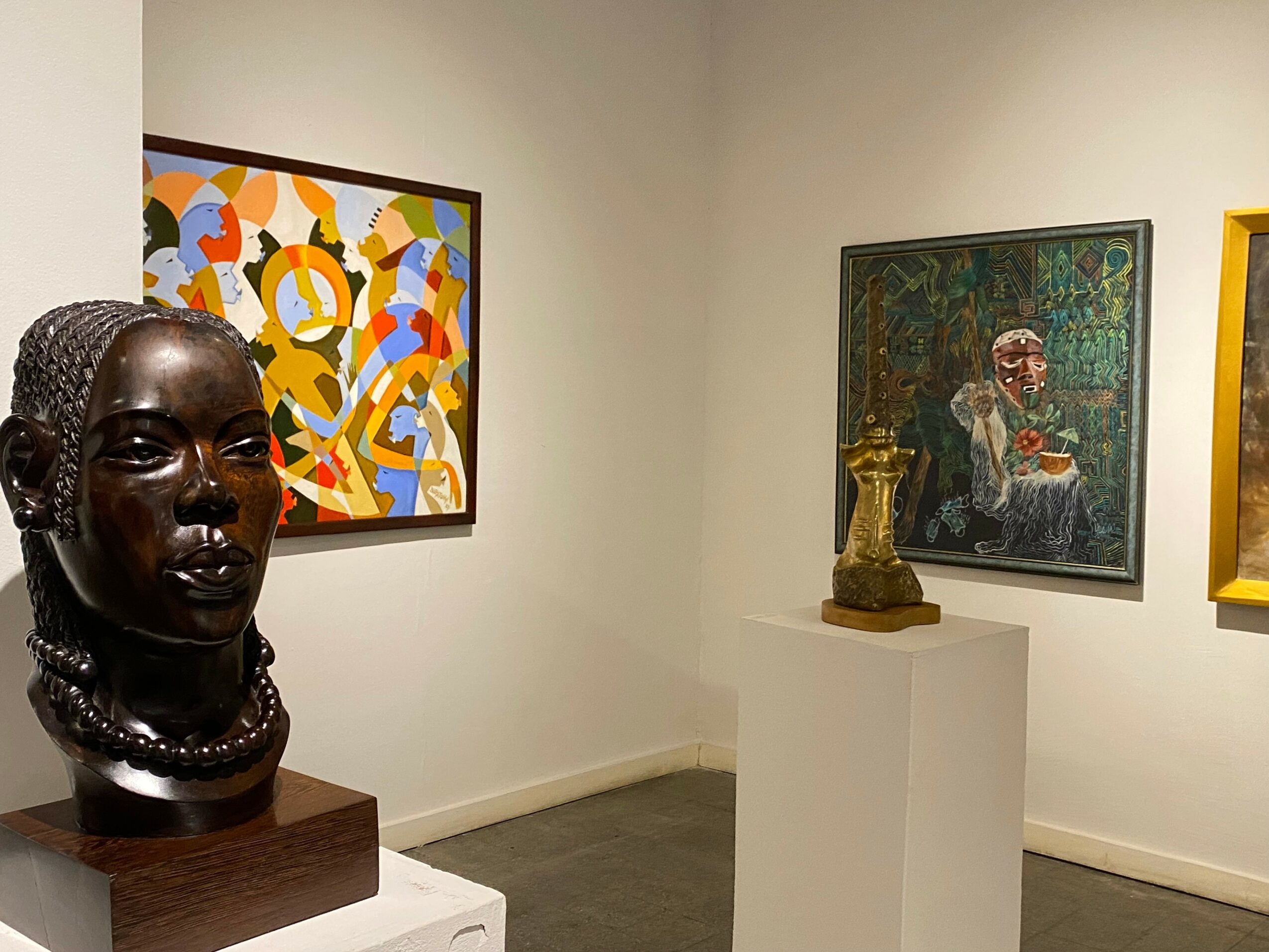 Art gallery with a dark bust sculpture, colorful abstract painting, and a seated woman painting on the wall.