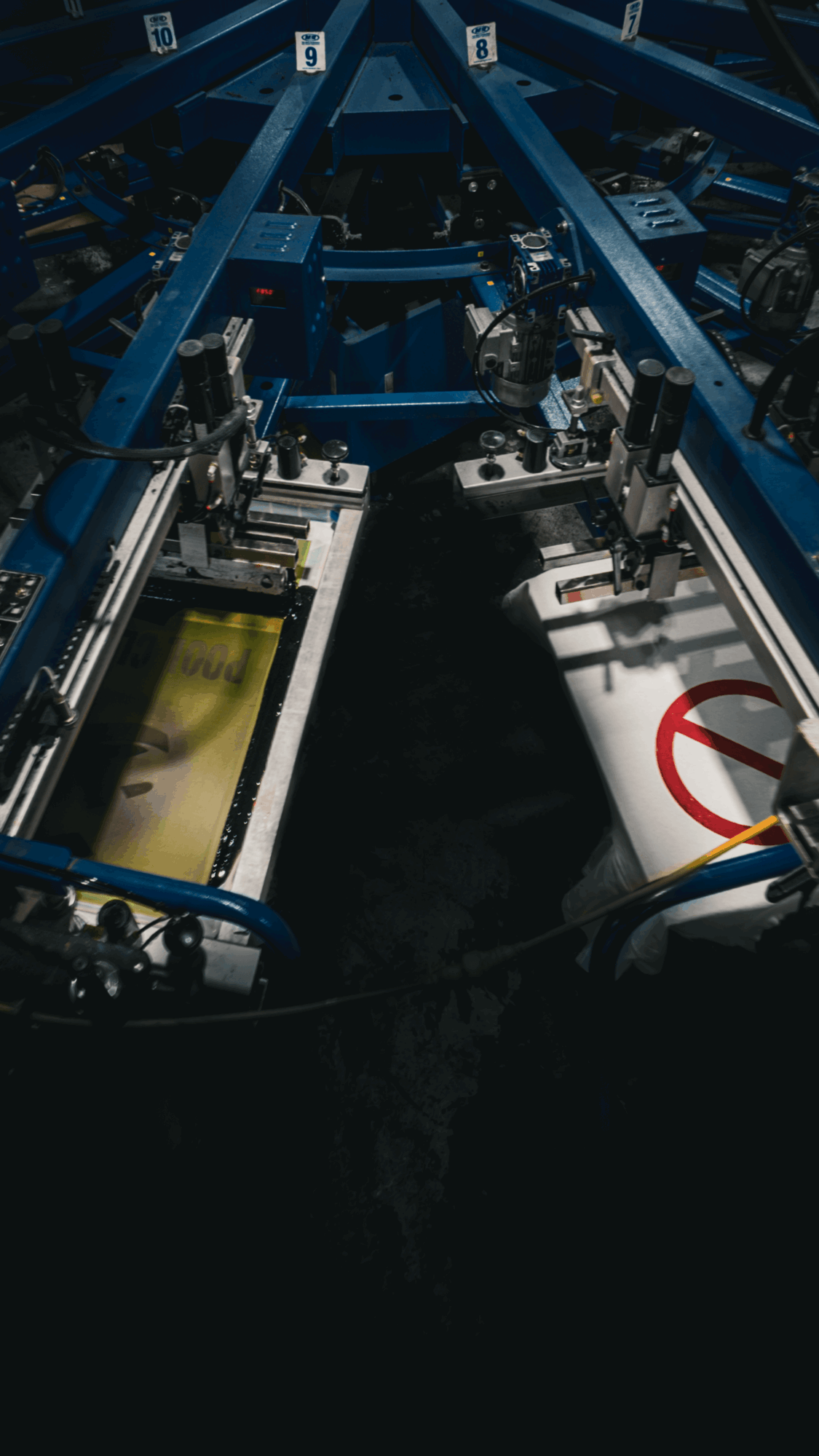 Industrial machinery with blue metal framework and two white panels, one with a red circle and slash symbol, in a dark environment.