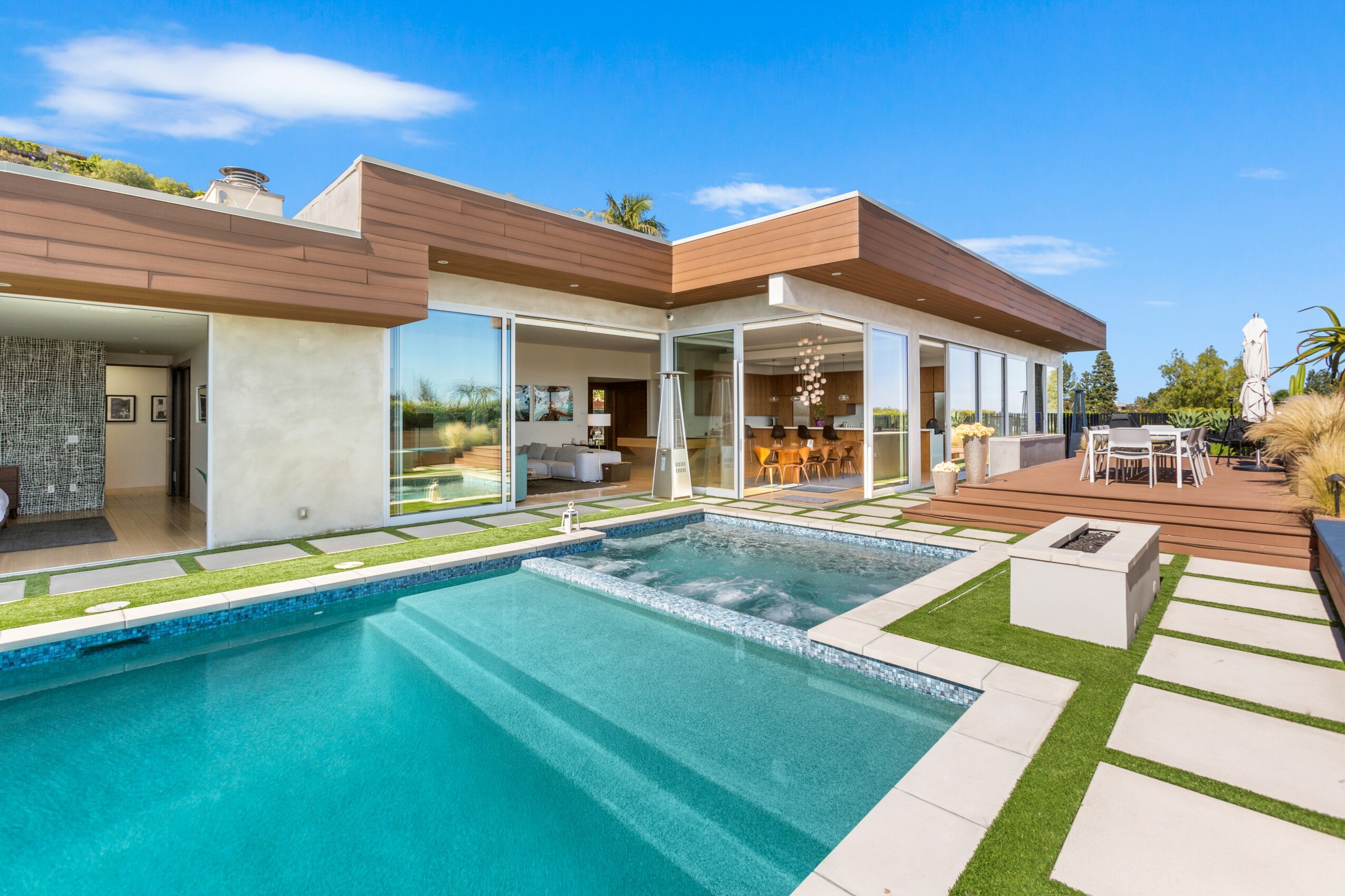 Modern house with large glass windows, outdoor pool, and patio area under a blue sky.