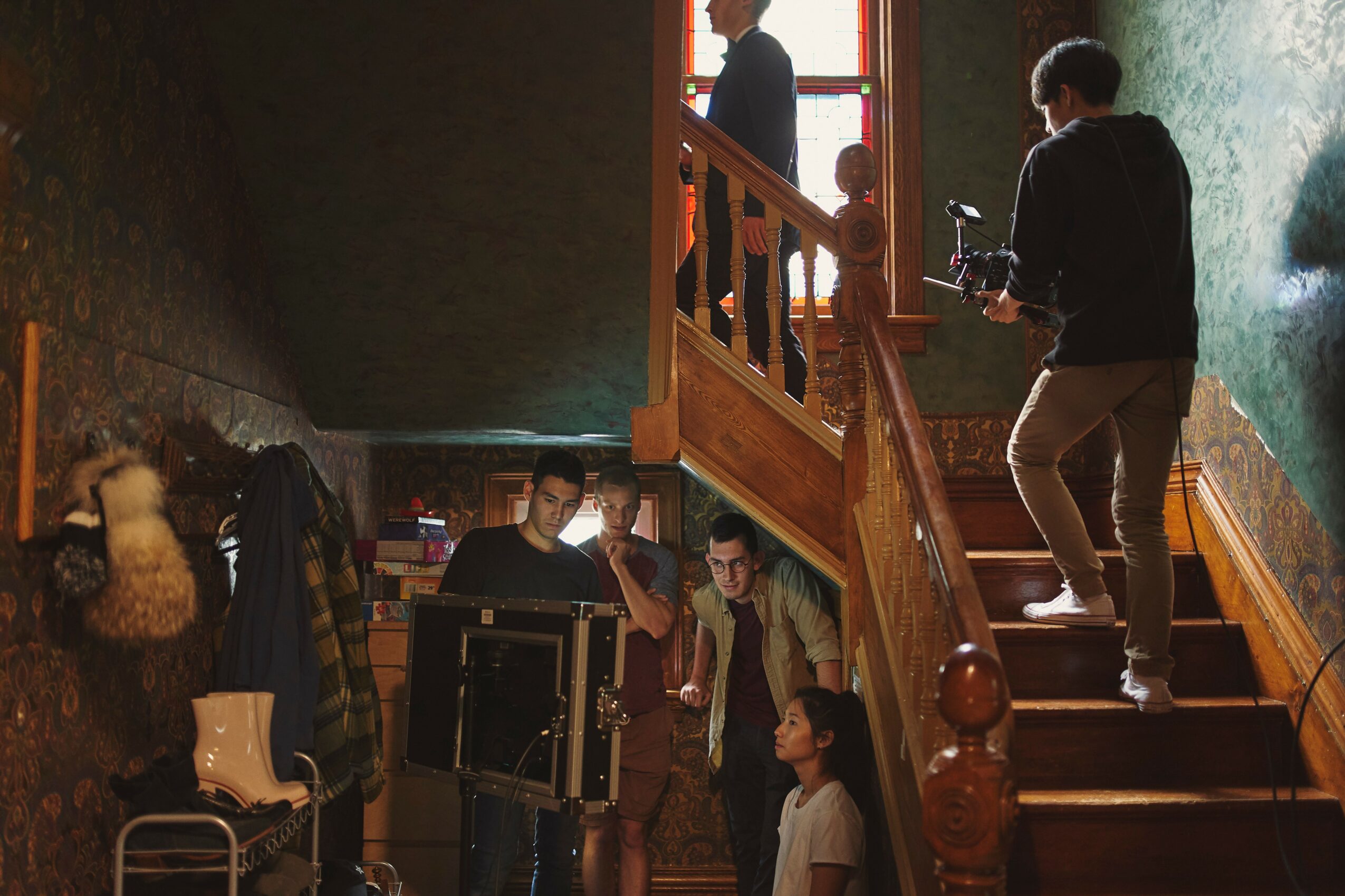 People on a staircase with a person holding a camera, others standing and sitting nearby, dimly lit interior.