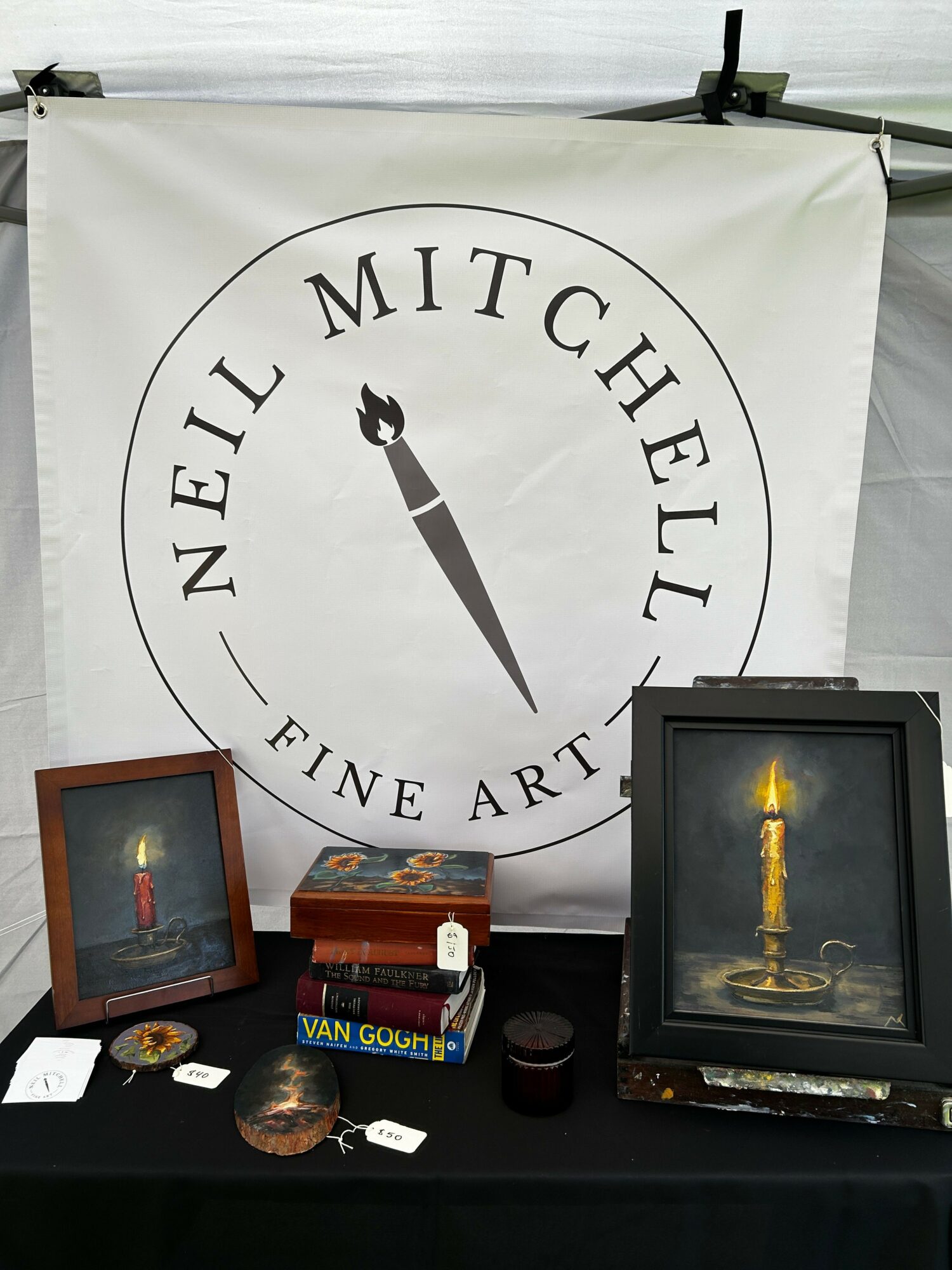 Display with a framed picture, a box, and a small object on a black surface, with a white banner in the background.