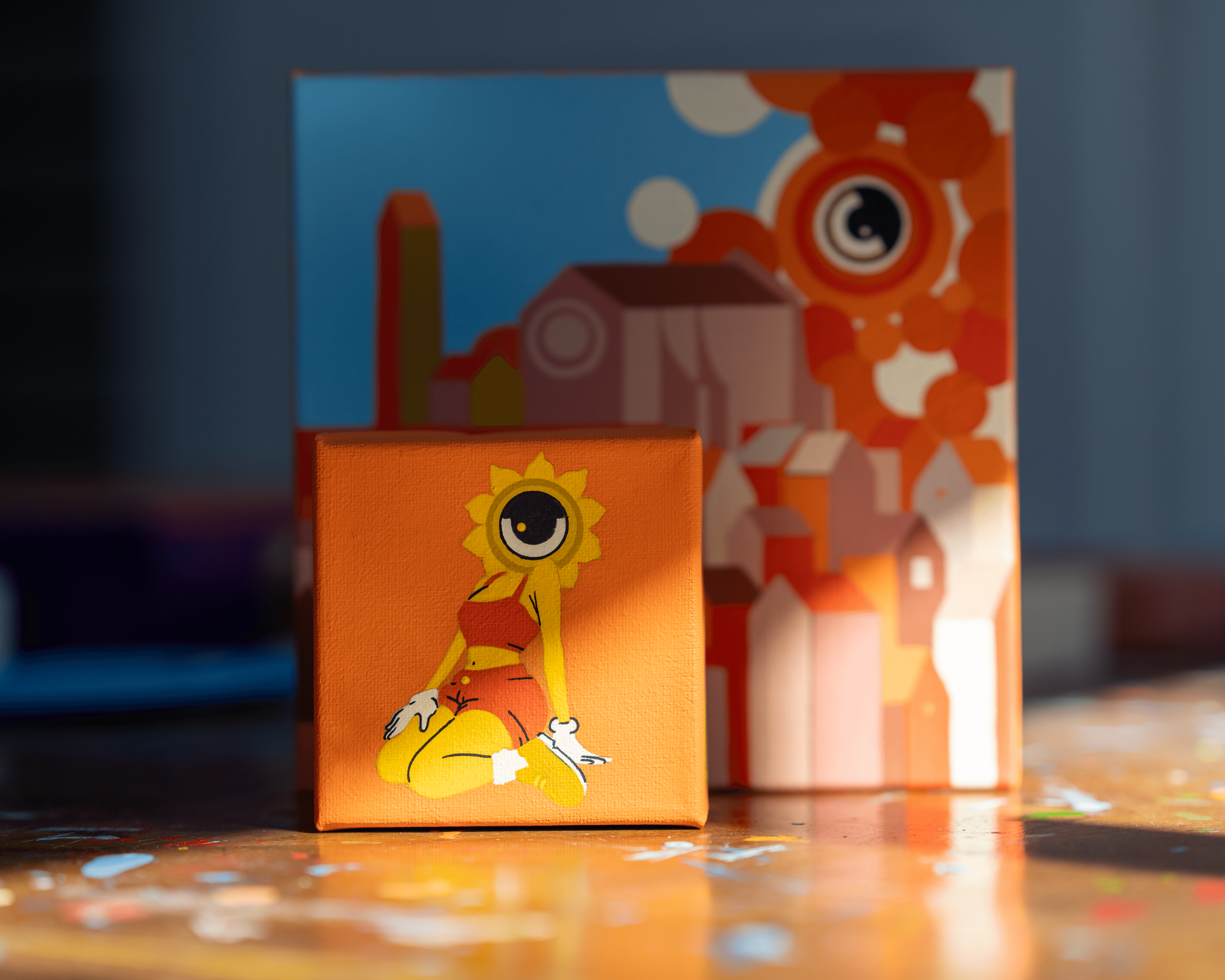 Small orange box with a cartoon character sitting cross-legged, wearing a yellow sun hat, holding a small object, with a colorful background.