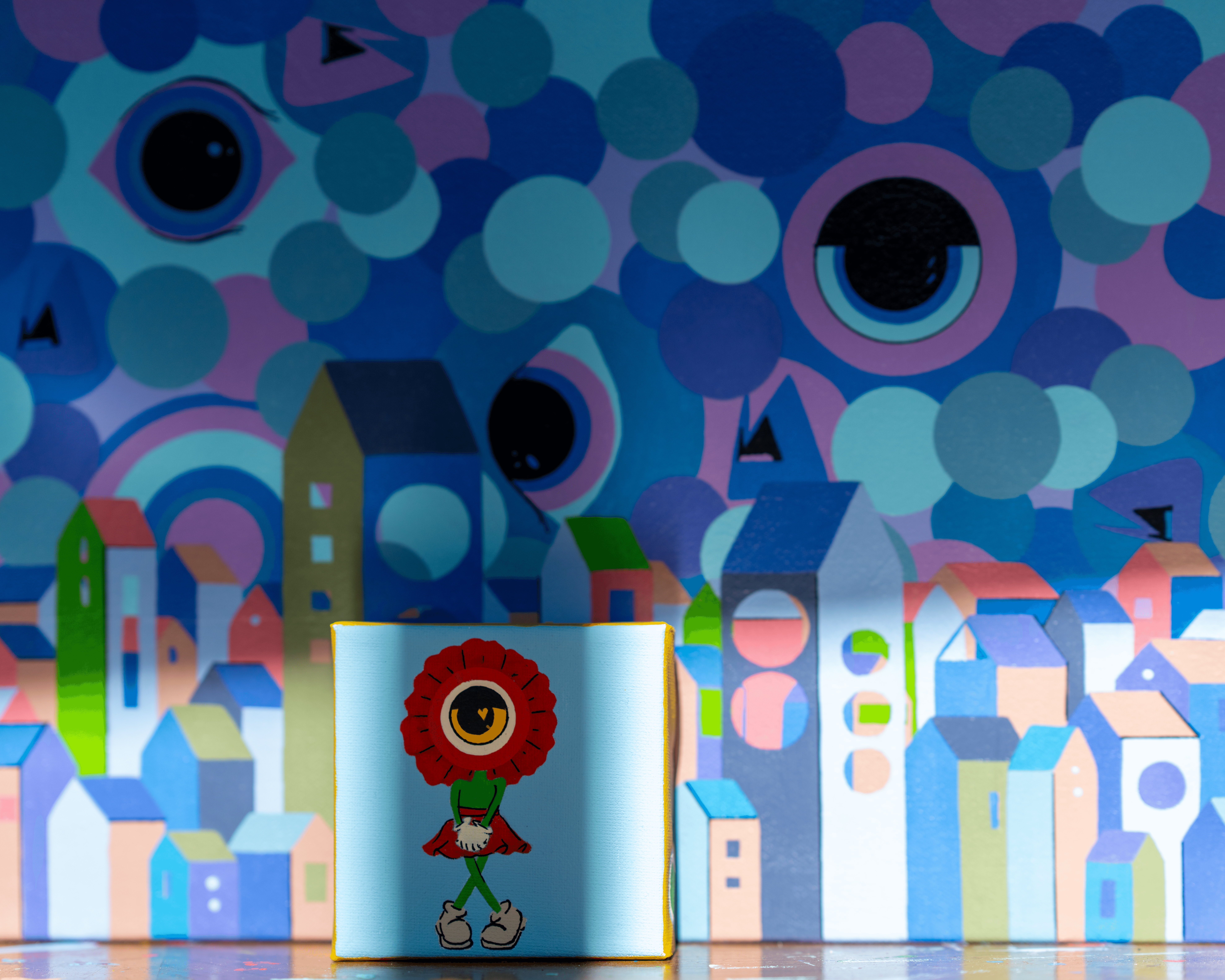 Colorful abstract background with a small puppet-like figure in front, featuring a red face and green body.