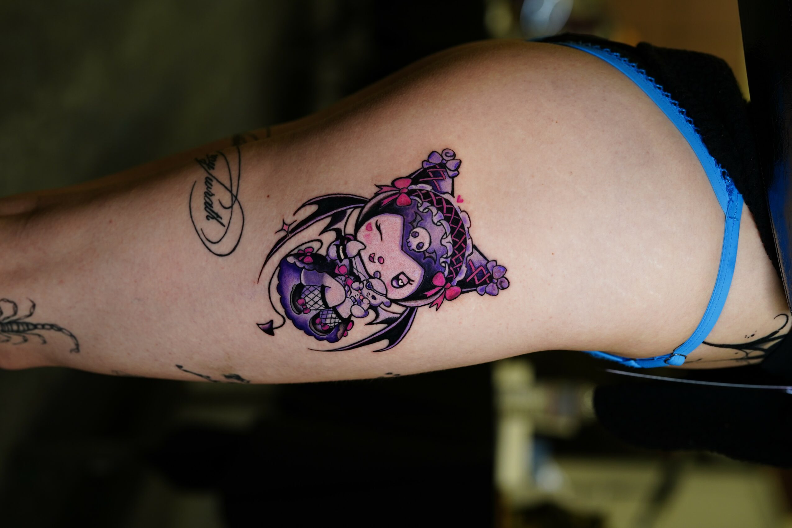 Tattoo of a cartoon girl with purple hair and accessories on person's thigh, with other tattoos visible nearby.