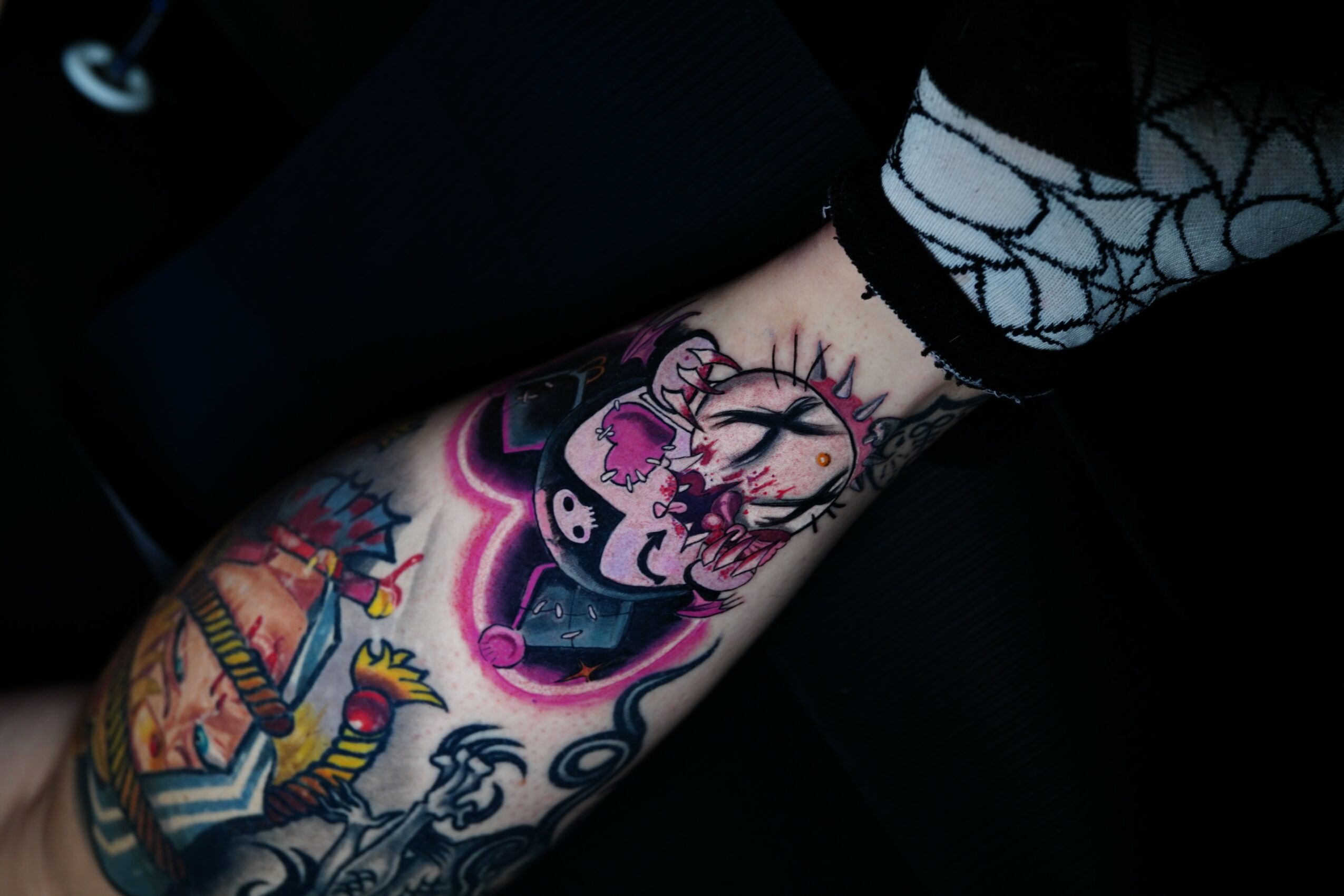 Tattooed arm with colorful designs, including a clock, a skull, and a rainbow, visible on a person's arm and clothing.